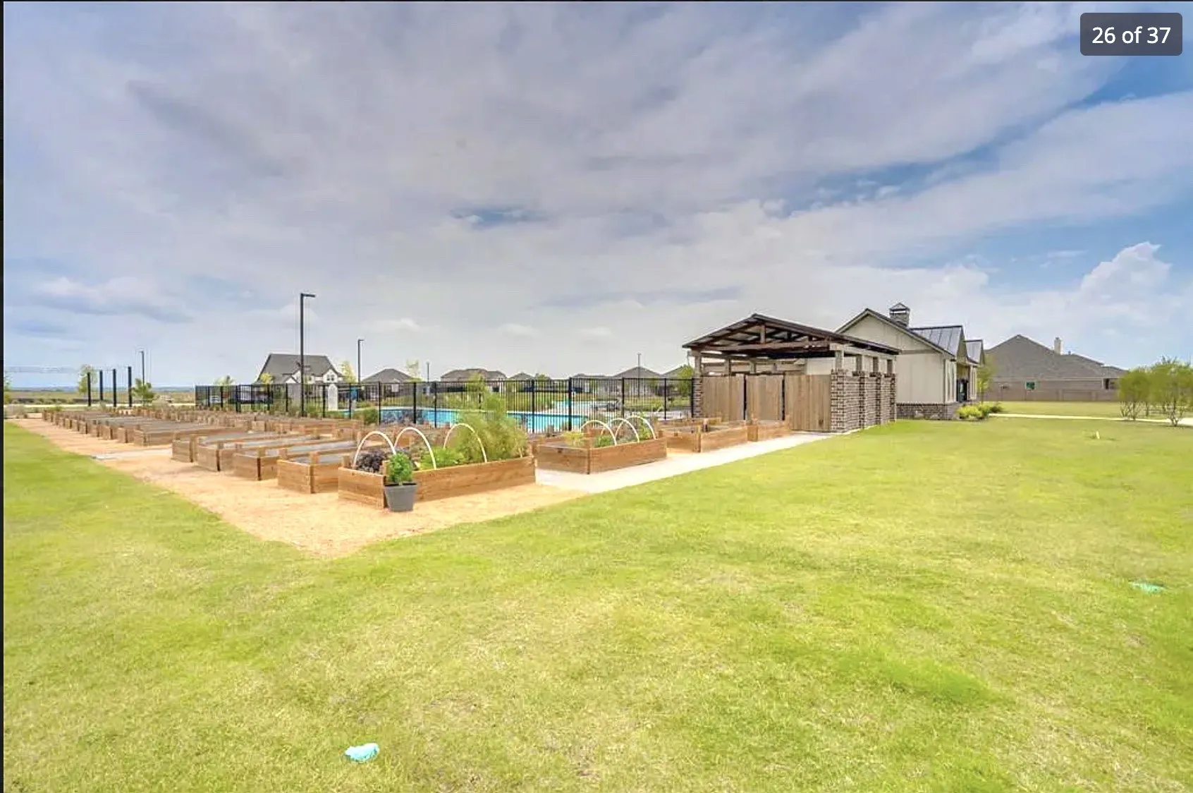 Community garden with multiple raised planters, adjacent to a structured pavilion and a swimming pool area