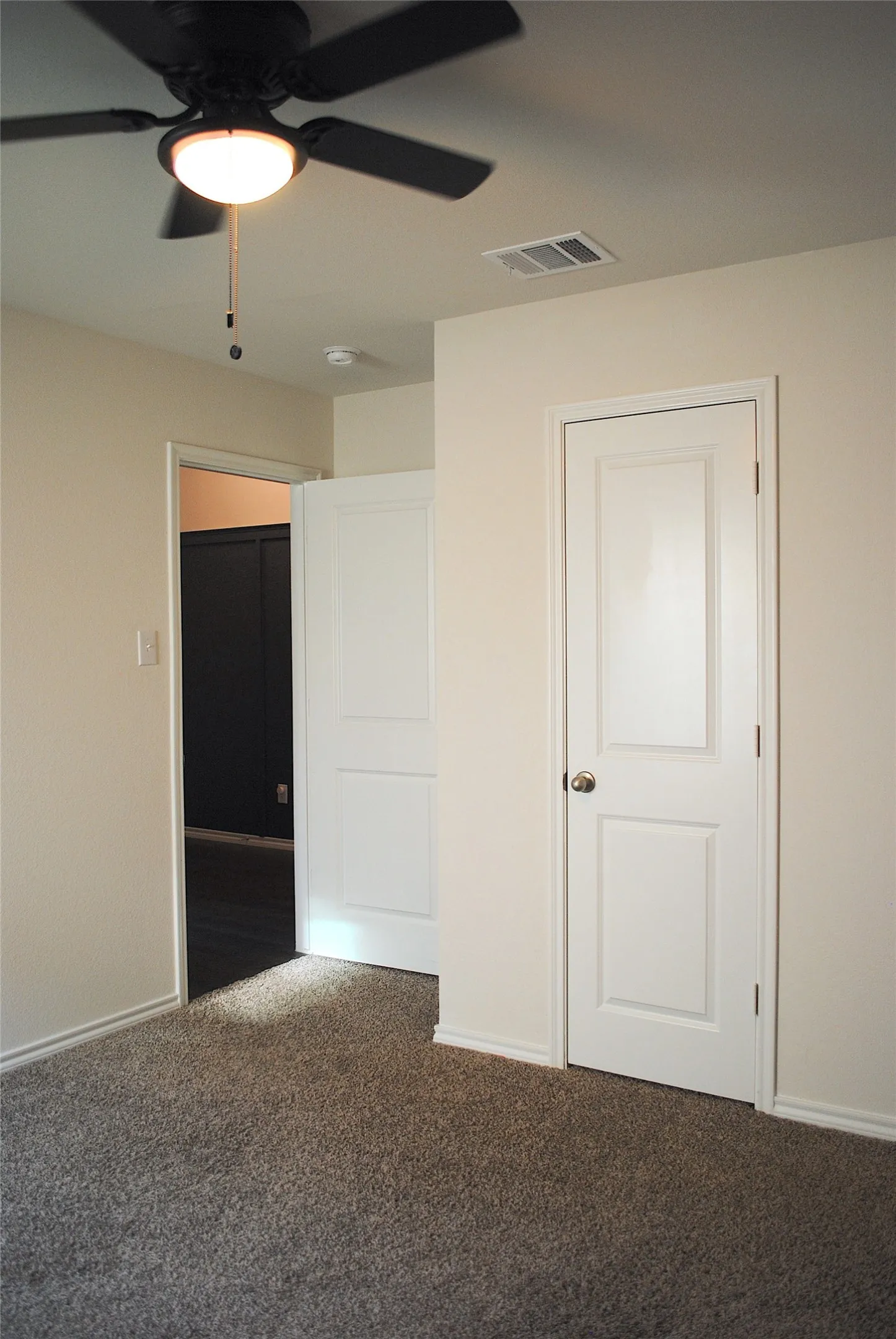 Neutral-toned walls, textured carpeting, a white paneled door, and a black ceiling fan with an integrated light fixture