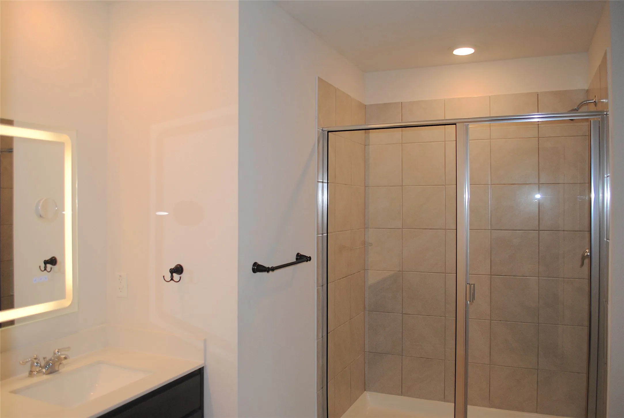 Vanity with integrated sink, rectangular illuminated mirror, and dark cabinetry