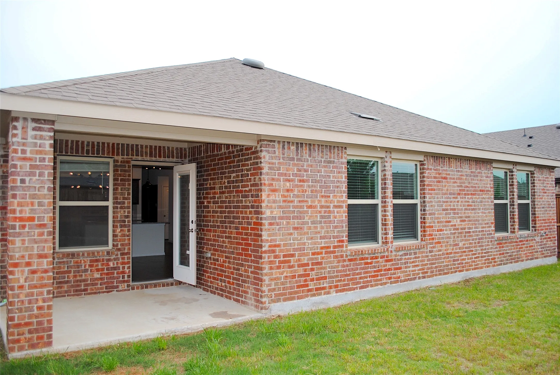 Brick exterior with covered patio, multiple windows, and a shingled roof