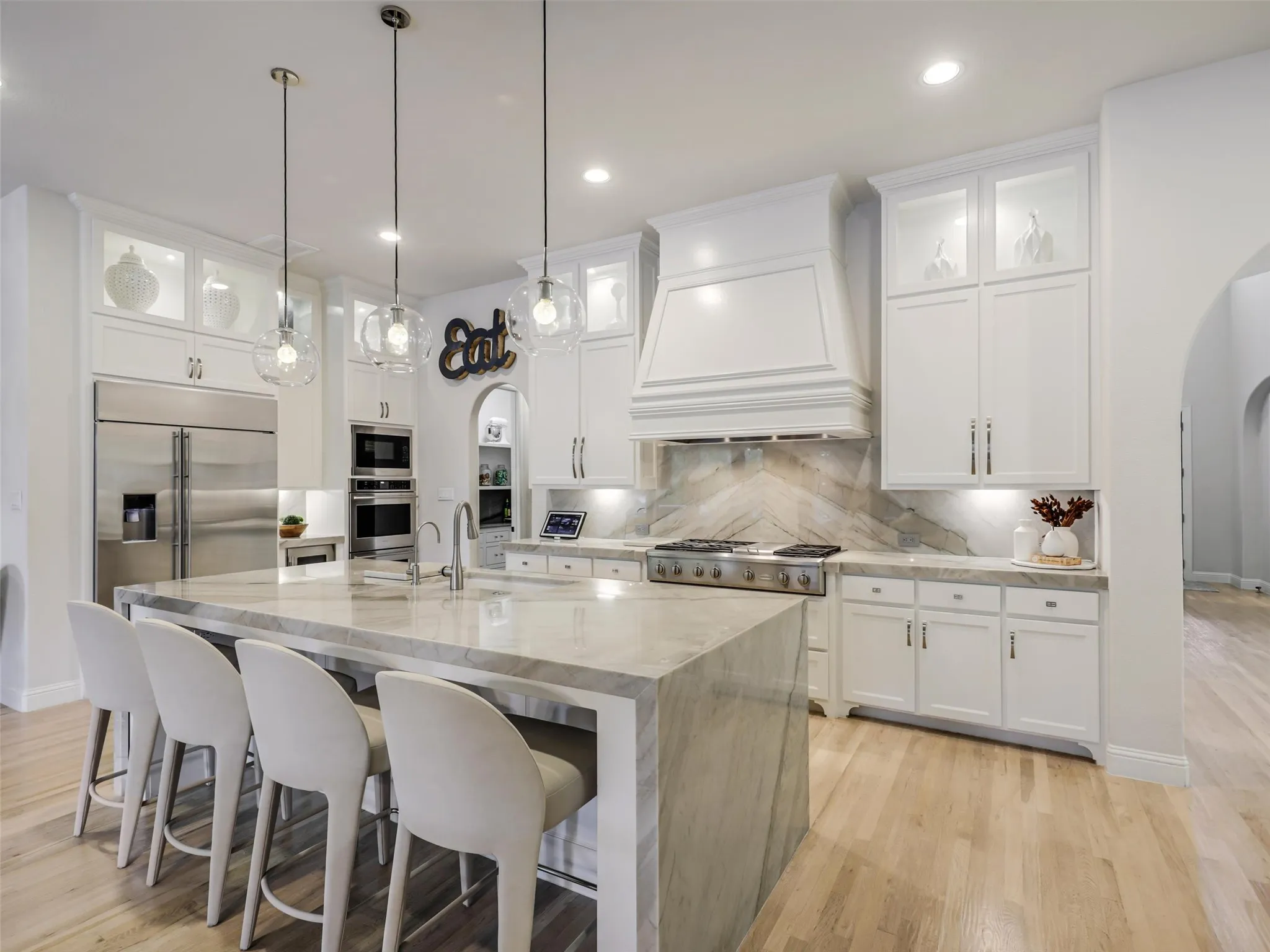 . Custom cabinetry provides abundant storage, while the oversized center island with breakfast bar offers additional prep and gathering space. Highend appliances include a built-in refrigerator, wine chiller, commercial-grade gas cooktop with vent hood, double ovens, and built-in microwave. • Quartzite waterfall countertops with matching quartzite backsplash
• Cabinets extended to the ceiling
• Custom pantry
• GE Monogram appliances: built-in refrigerator, double oven, and 48 inch range
• Built-in ice machine and wine refrigerator