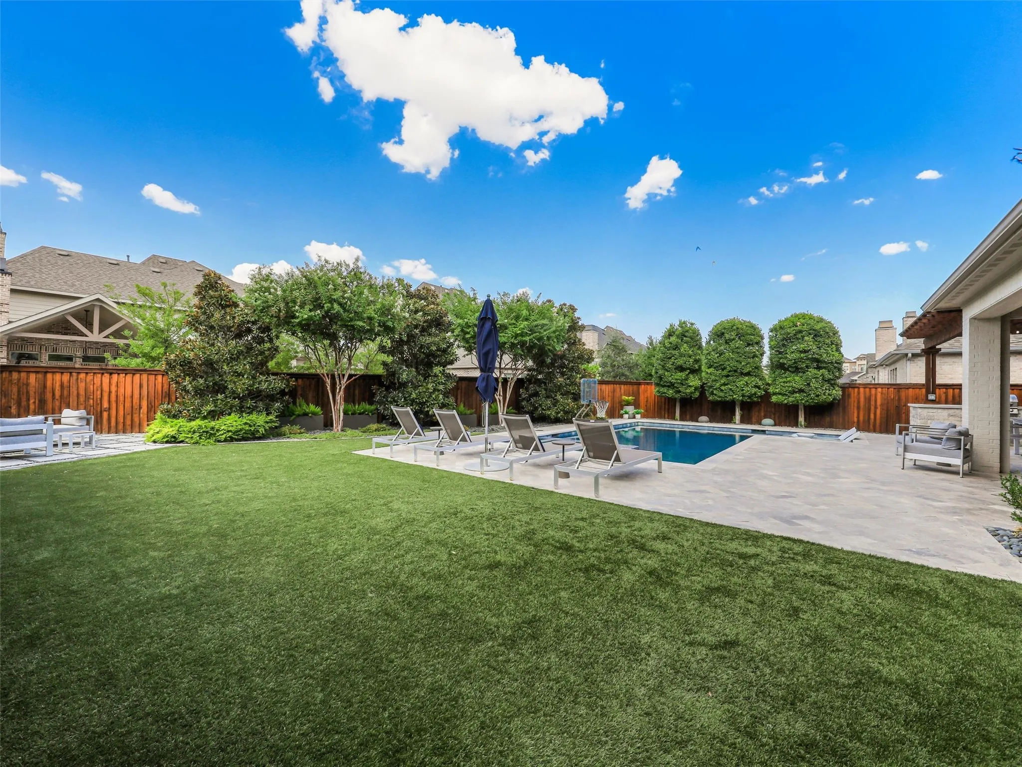 Beyond the pool, the fully fenced backyard features low-maintenance turf landscaping and a separate fire pit patio, creating multiple outdoor gathering spaces for entertaining, relaxing, and enjoying evenings at home. • Custom pool and spa ranging from 3.5 ft in the shallow end to 6 ft in the deep end, with basketball hoop
• Baja shelf with lounge chaises and table
• 5 Jandy pool lights, recently replaced
• Silver travertine decking throughout pool and patio
• Pergola over outdoor living area
• Built-in outdoor kitchen with Bull grill and Bull refrigerator
• Fire pit patio
• Artificial turf, approx. 21 ft x 38 ft
• Mature landscaping with landscape lighting
• Decorative rock: approx. 15 tons of large Texas black rock and 3 tons of black Mexican river stone
• Built-in speakers in the patio ceiling and throughout the pool and landscape areas