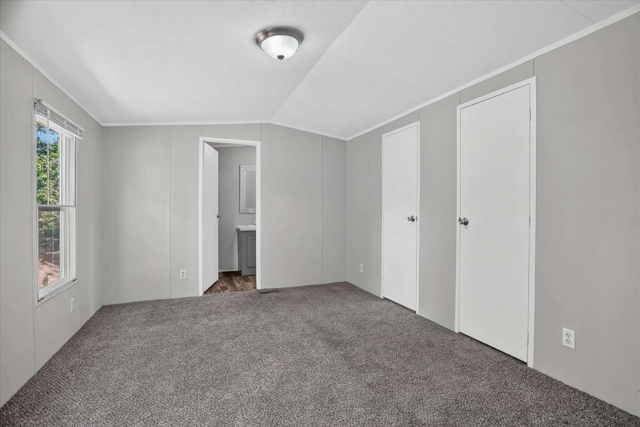 Gray wall paneling with white trim, gray carpet flooring, and a single window with blinds