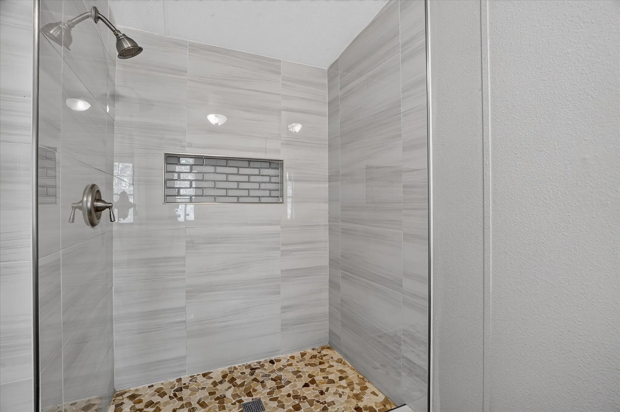 Walk-in shower with clear glass enclosure, stone tile flooring, large format tile walls, recessed lighting, and a subway tile accent niche