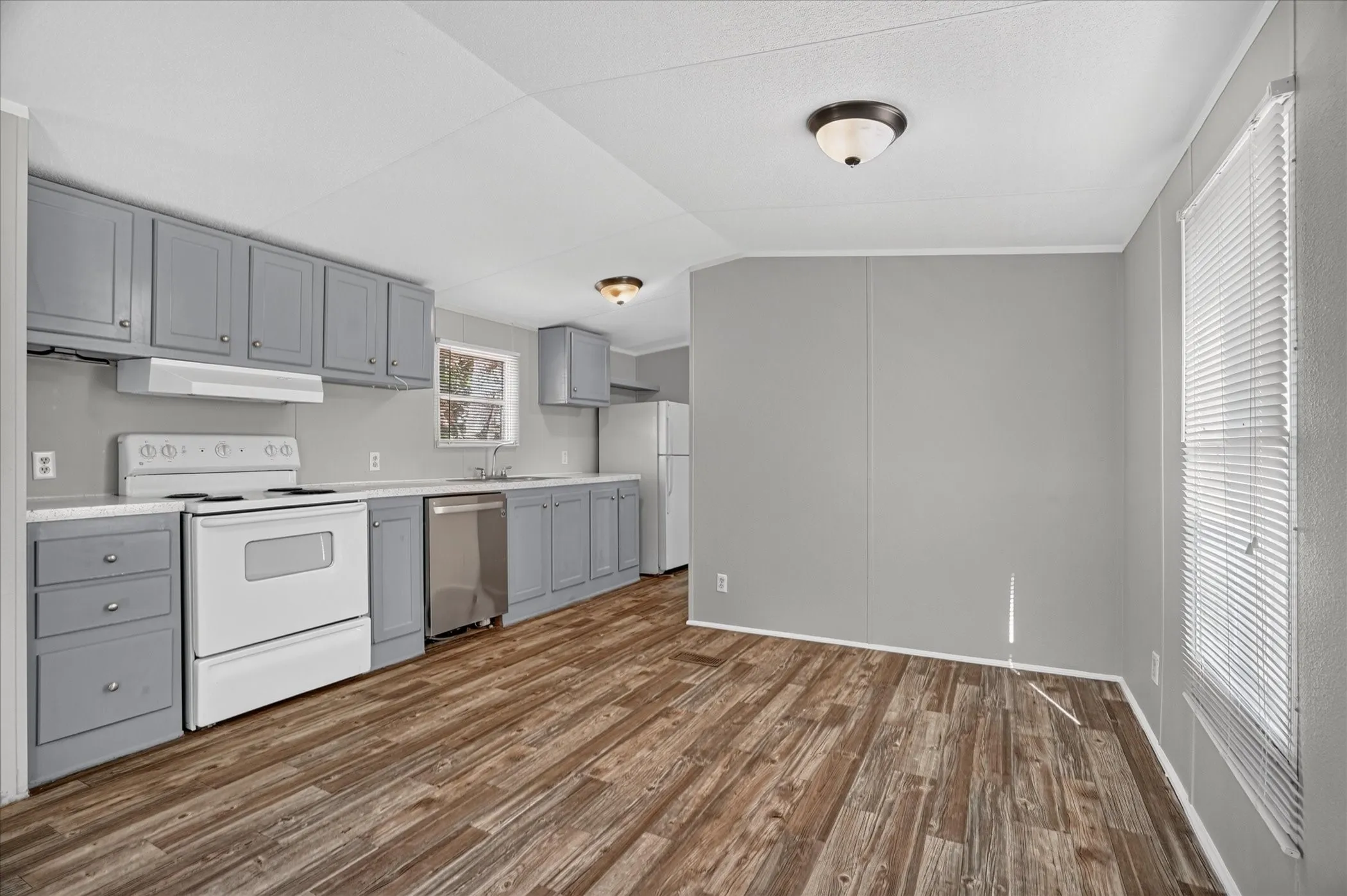Kitchen featuring wood-finish flooring, gray cabinetry, white countertops, and white appliances