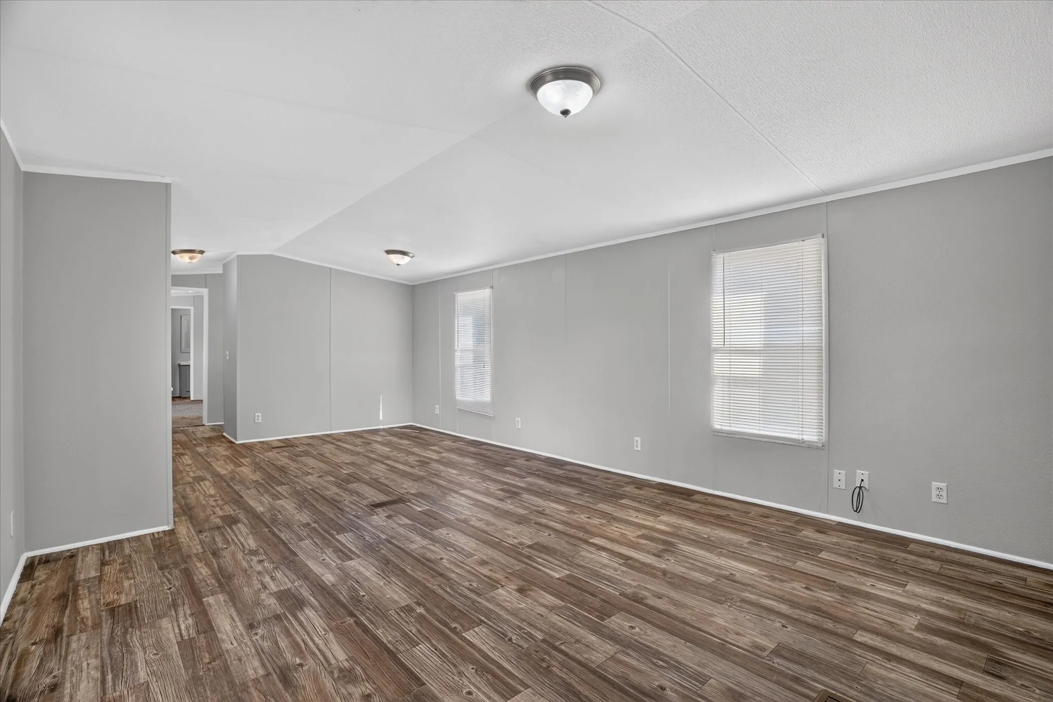 Wood-finish flooring with light gray walls, multiple flush-mount ceiling lights, and windows with blinds