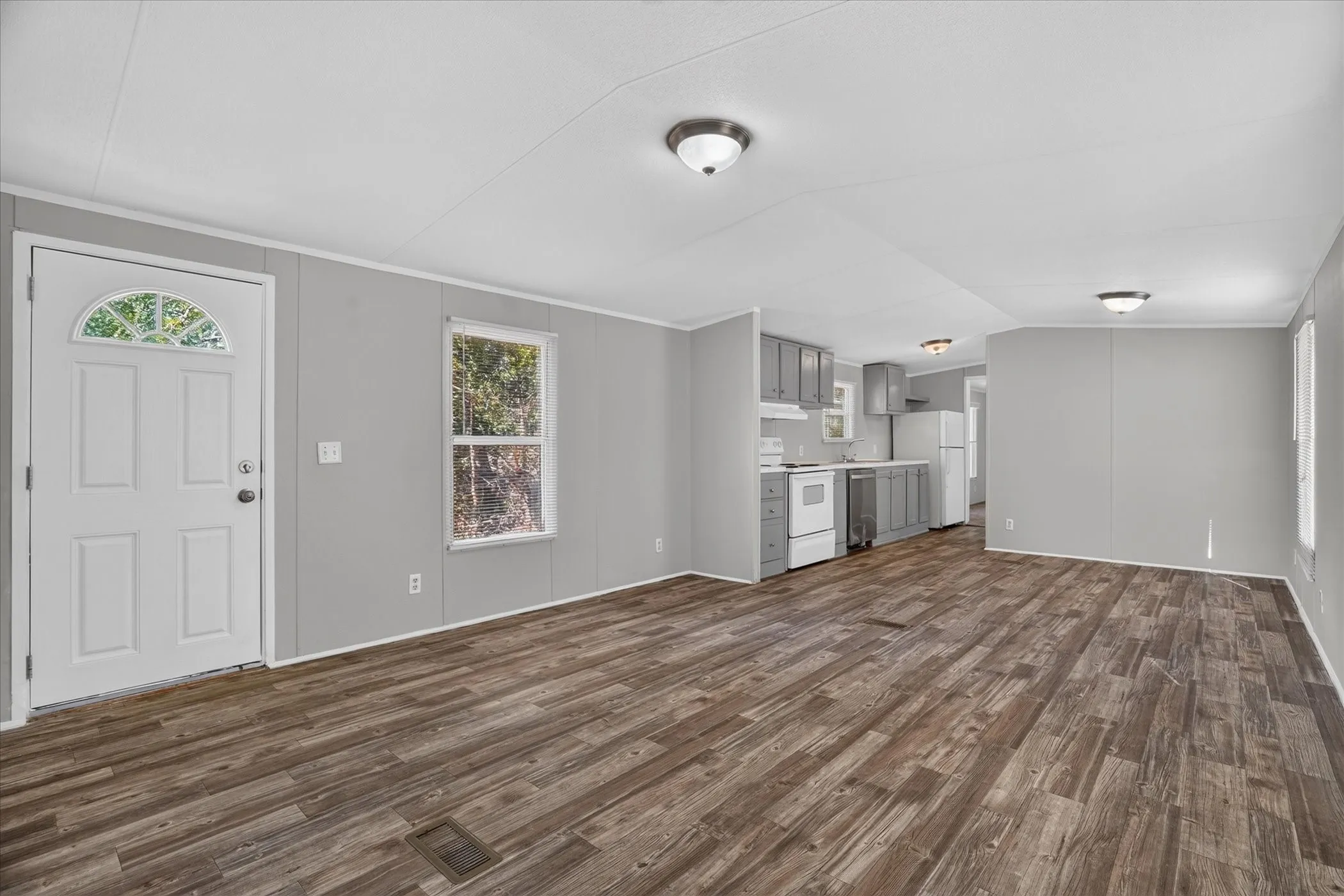 Open-concept living space featuring wood-finish flooring, a white front door with an arched glass panel, and recessed lighting