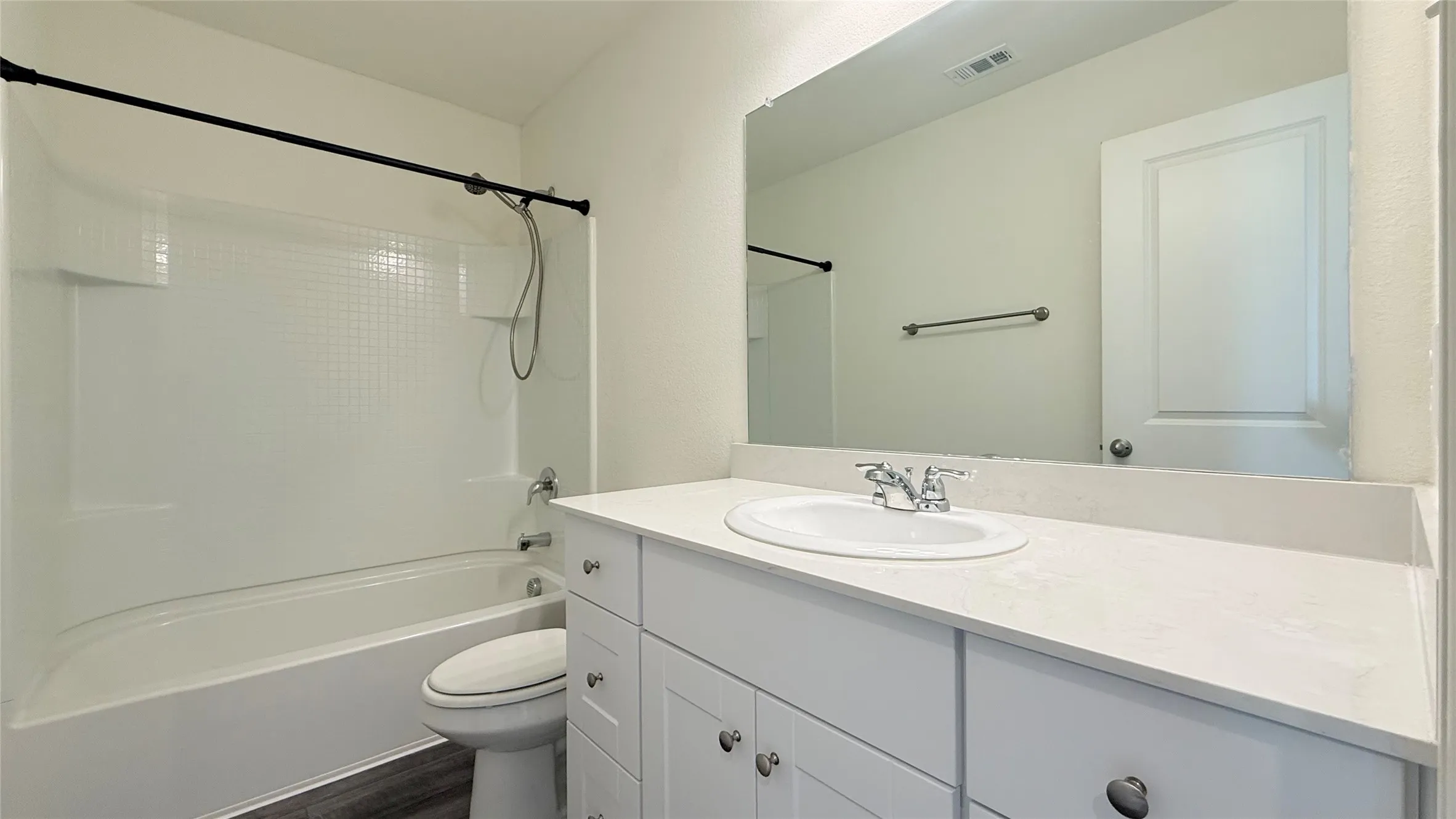 White vanity with an integrated sink and chrome faucet, large frameless mirror, and a white bathtub/shower combination with a black shower rod