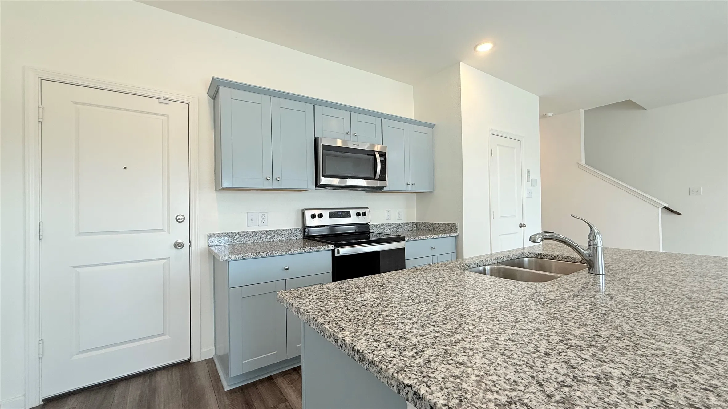 Kitchen featuring light blue cabinetry, stainless steel microwave, electric range, and speckled countertops