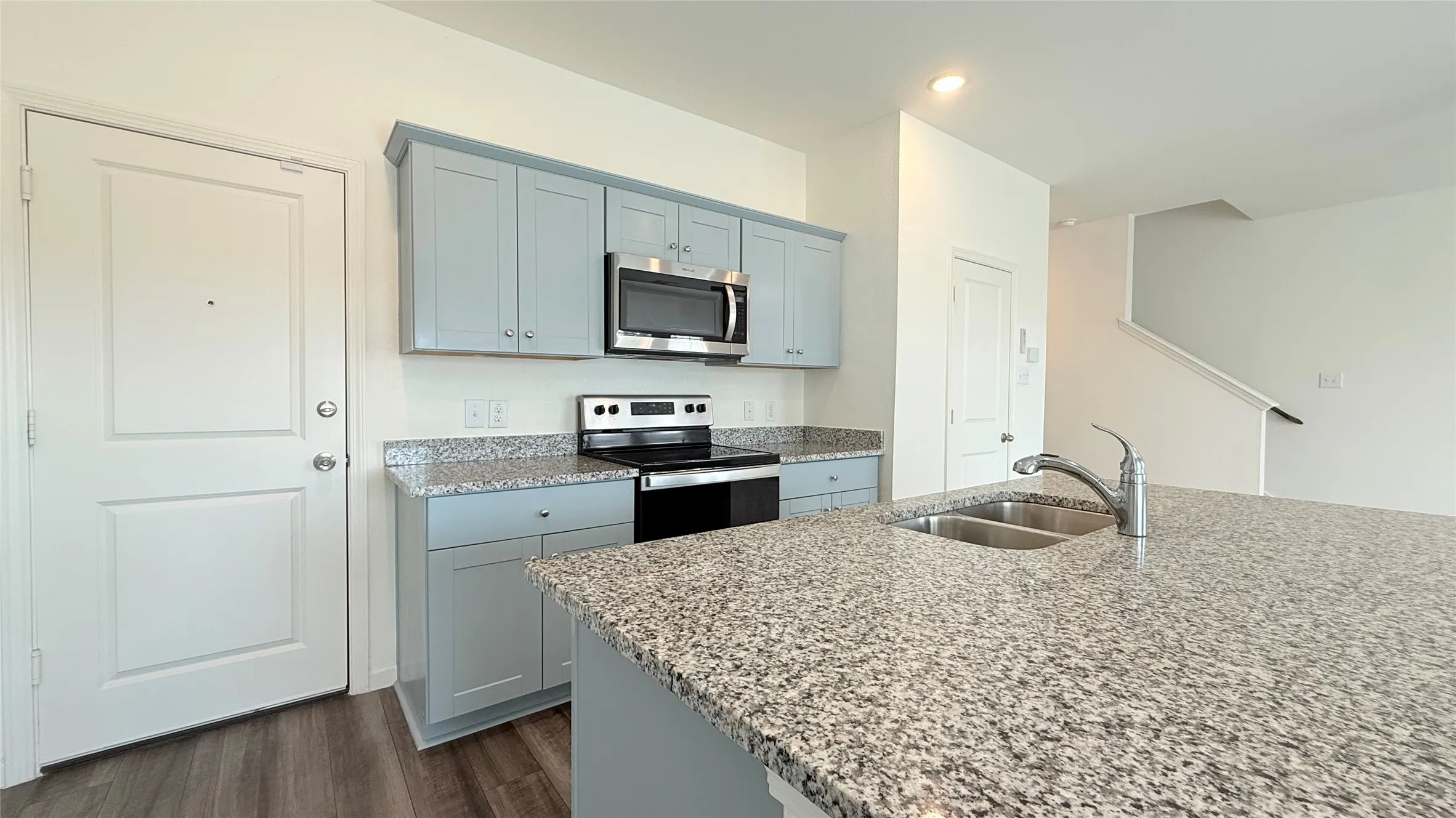 Kitchen featuring a dual basin sink, integrated oven range, built-in microwave, and light-colored cabinetry with a stone-finish countertop