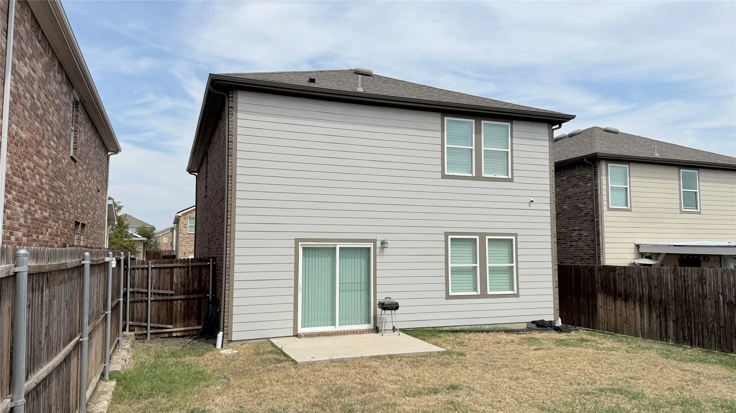 Two-story property featuring light gray siding with contrasting trim, a dark shingle roof, and a concrete patio