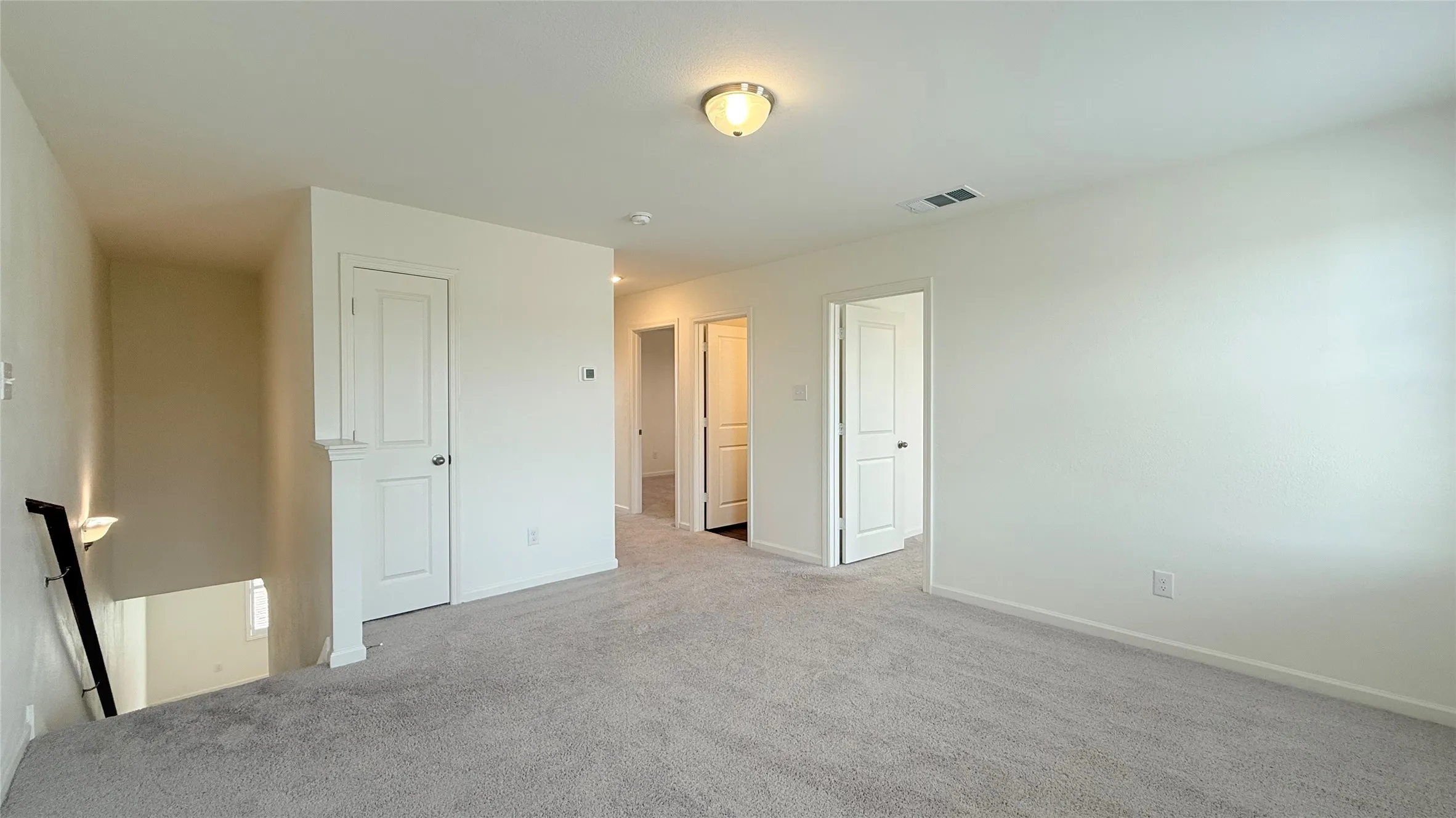 Expansive carpeted area with white walls, multiple doorways, and an overhead flush-mount light fixture