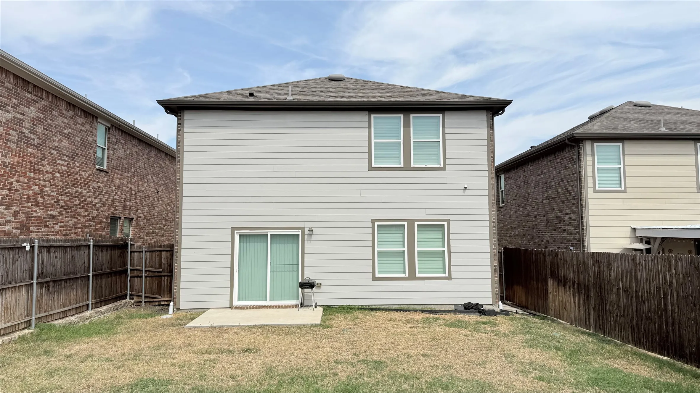Two-story residence featuring siding, a sliding glass door, multiple windows, and a concrete patio
