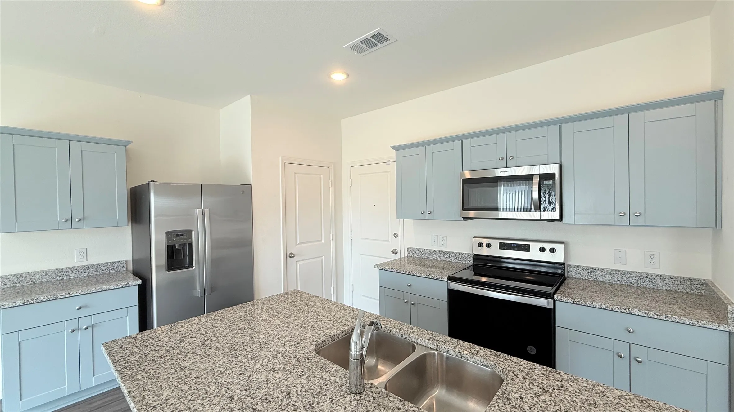Kitchen with light blue cabinetry, stainless steel appliances, speckled stone countertops, and a double basin sink