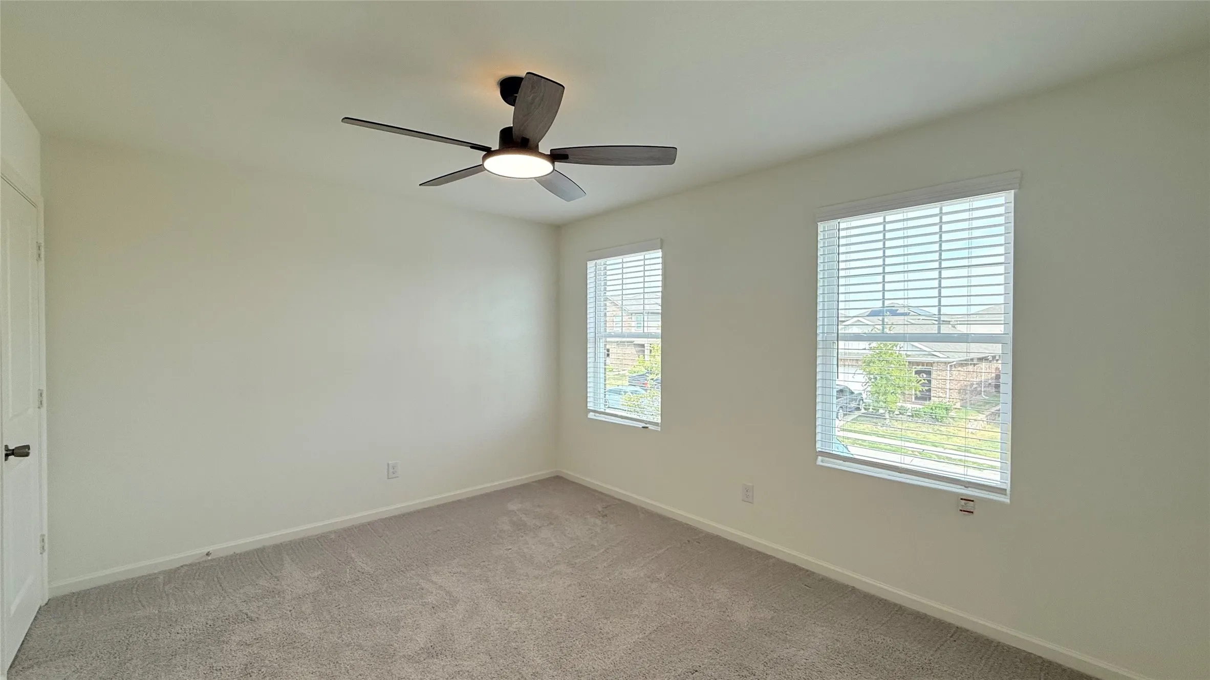 Light-colored walls, ceiling fan with integrated lighting, two windows with blinds, and light-colored carpeting