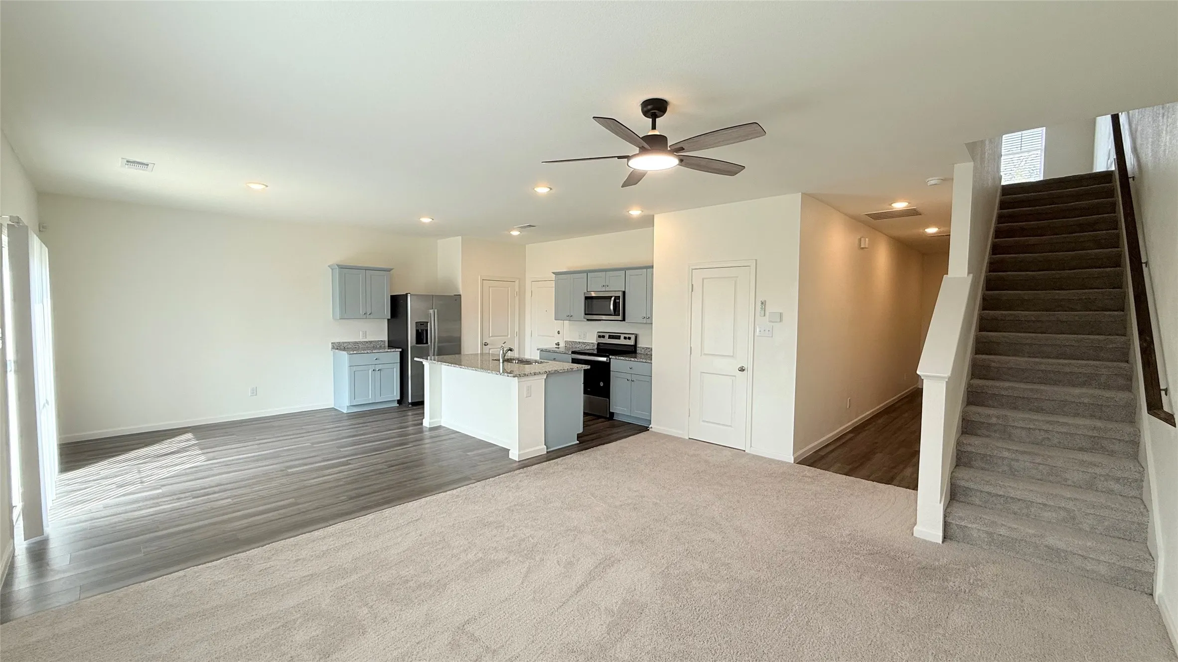 Open-concept living area featuring a kitchen with light blue cabinetry, an island with countertop seating, stainless steel appliances, and recessed lighting