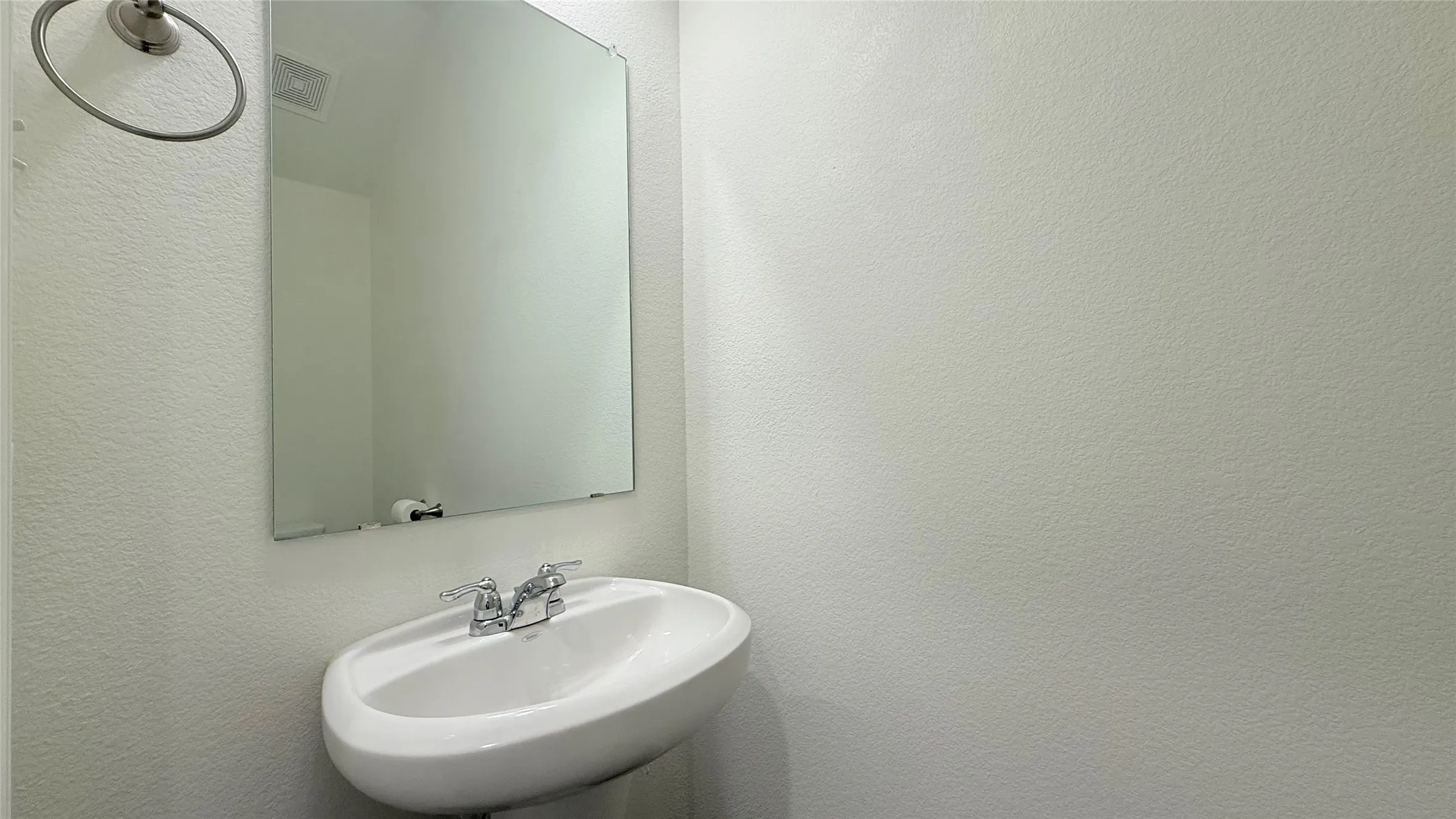 Pedestal sink with chrome faucet, framed mirror, and wall-mounted towel ring