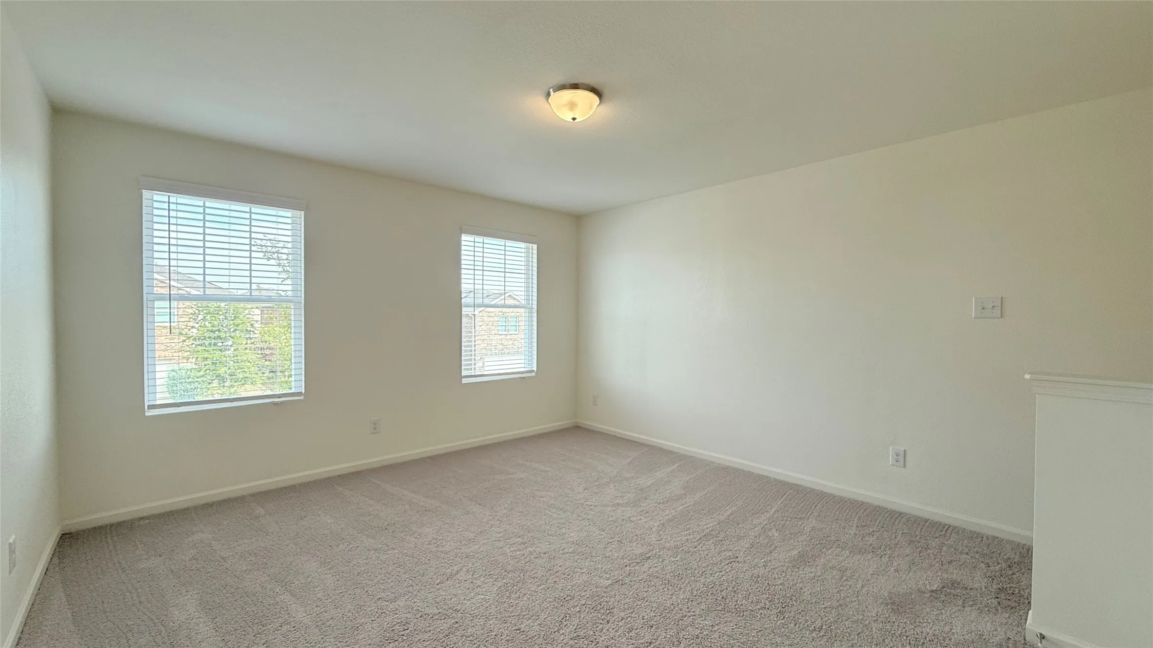 Carpeted room with two windows featuring blinds, neutral wall paint, and a flush-mount ceiling light fixture