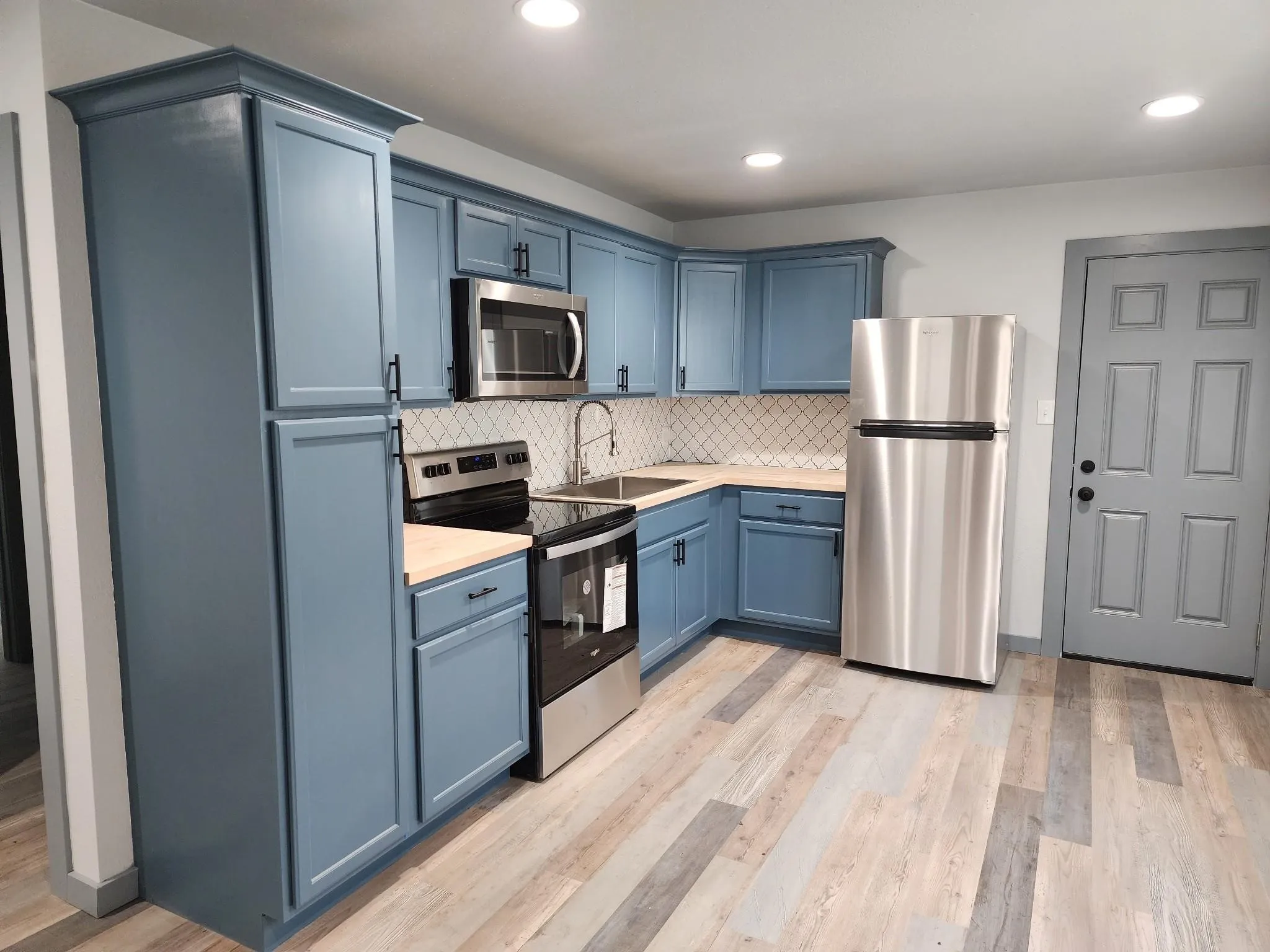 Kitchen featuring contemporary blue cabinetry, stainless steel appliances, wood-finish flooring, and a patterned tile backsplash