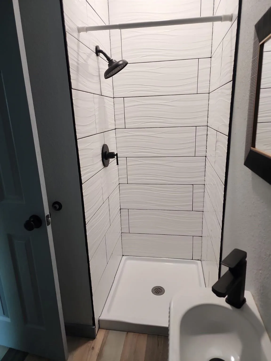 Walk-in shower with textured subway tile surround, matte black shower fixtures, and a white shower pan