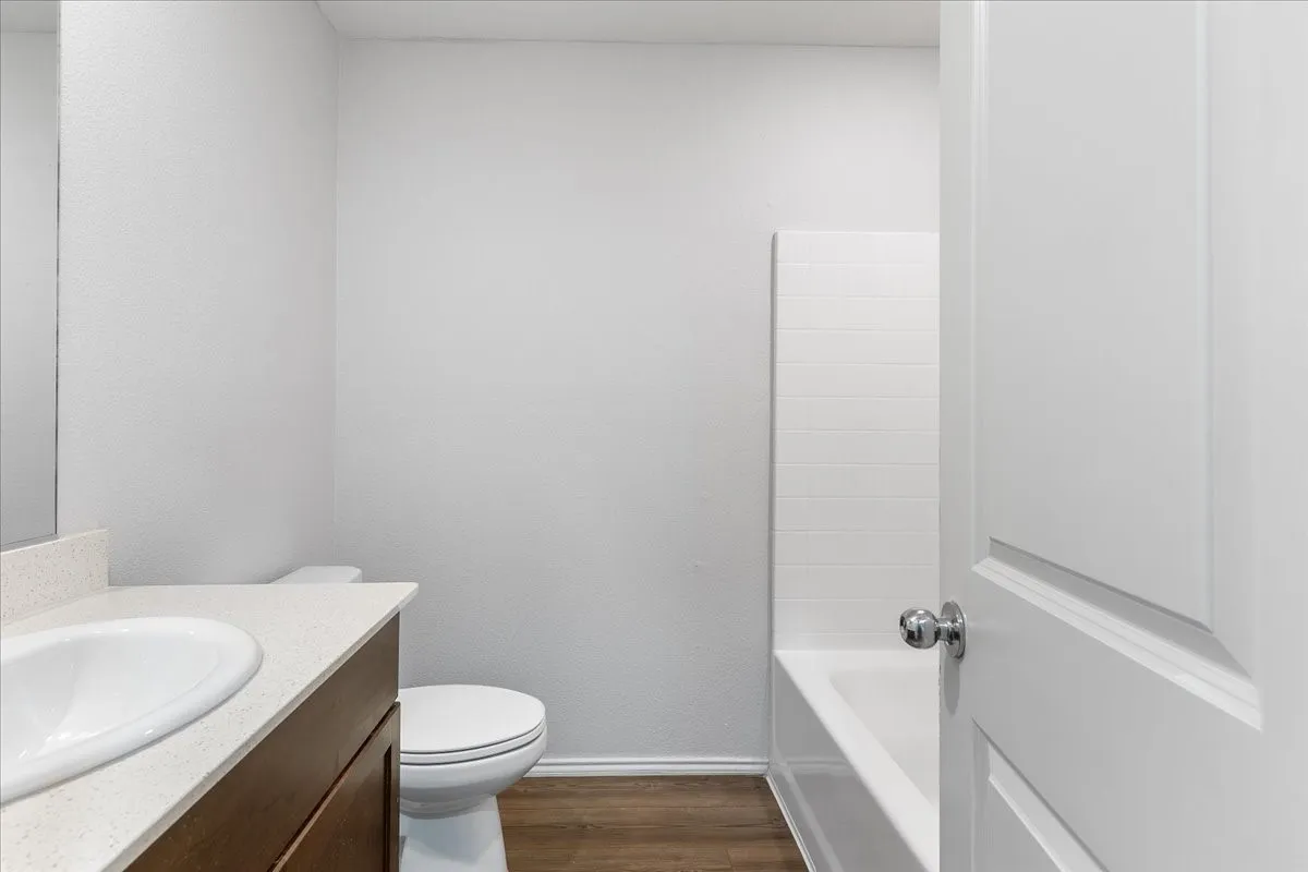 Wood-finish flooring, built-in vanity with light-toned countertop, integrated basin sink, and a tiled tub surround