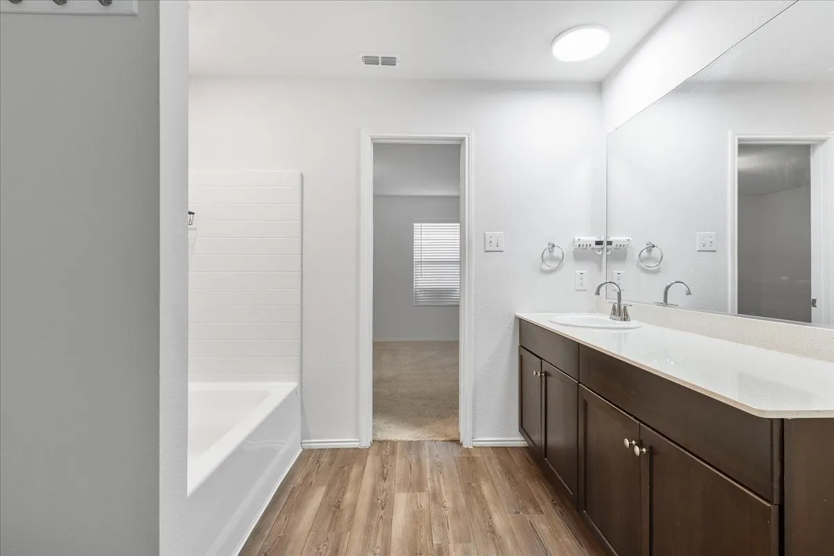 Bathroom featuring wood-finish flooring, a white bathtub with subway tile surround, and a vanity with a white countertop and dark wood-finish cabinetry