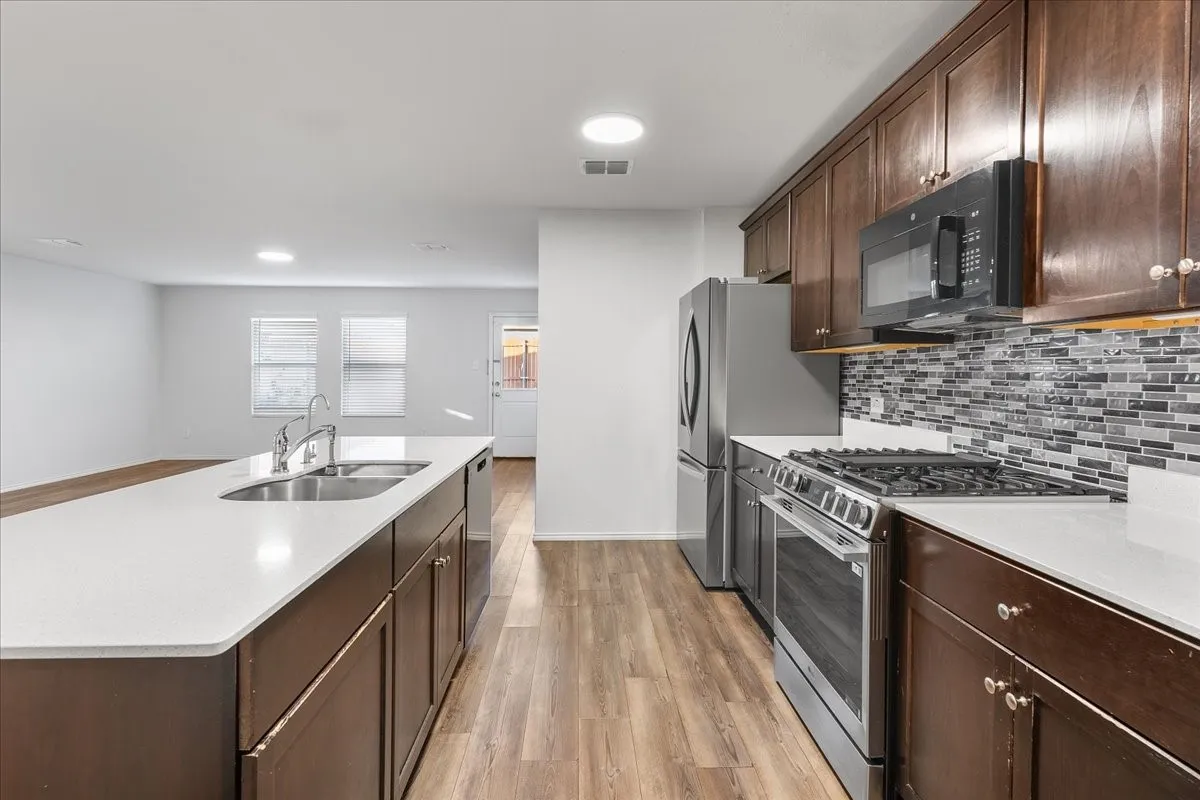 Kitchen featuring wood-finish flooring, dark wood cabinetry, white countertops, stainless steel appliances, and a mosaic tile backsplash