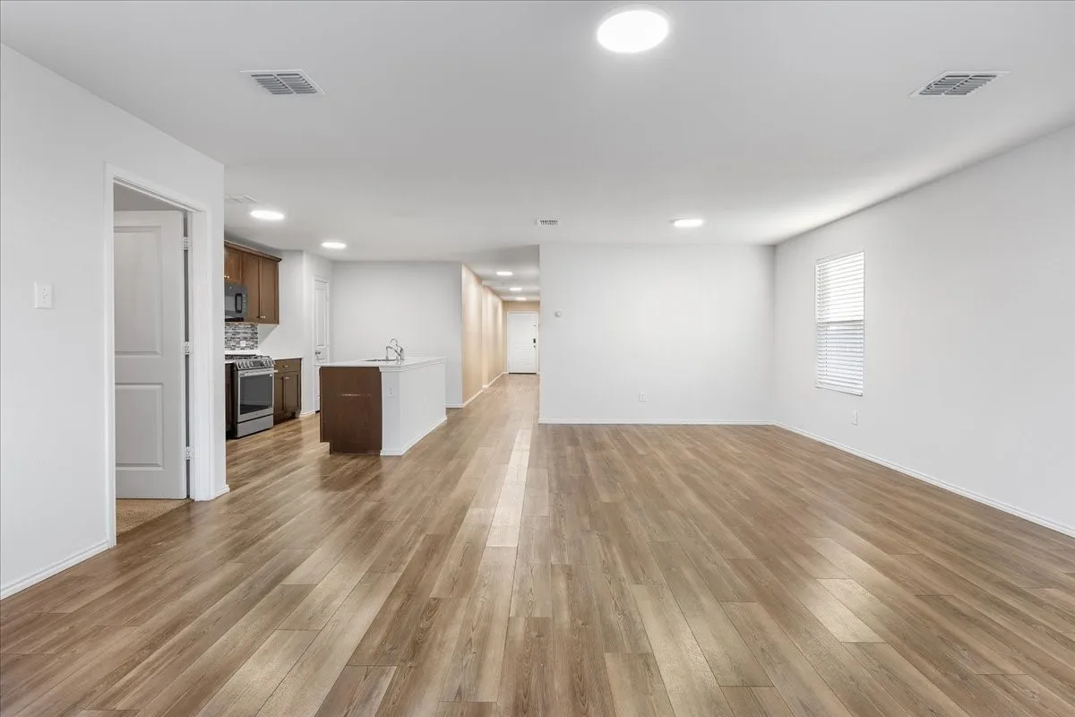 Open-concept living area with wood-finish flooring, white walls, recessed lighting, and a kitchen island with a built-in sink