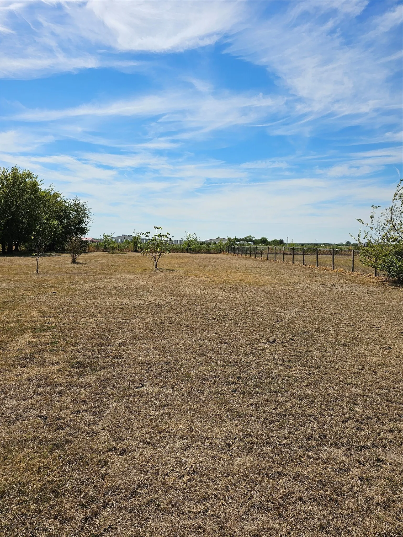 Expansive open lot featuring a clear sky, natural terrain, and perimeter fencing