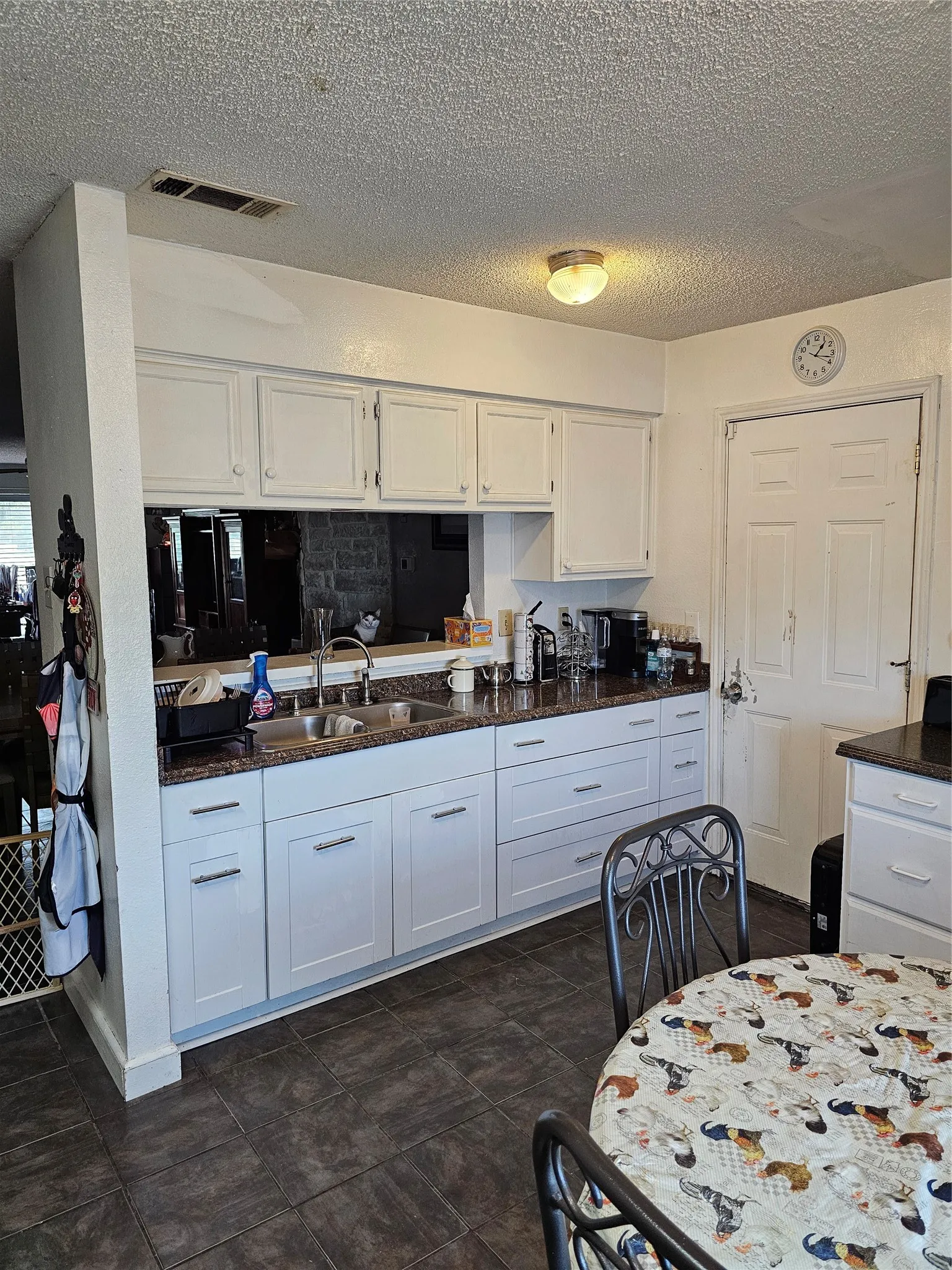 White cabinetry with silver-tone hardware, dark countertop, dual basin sink, and tile flooring