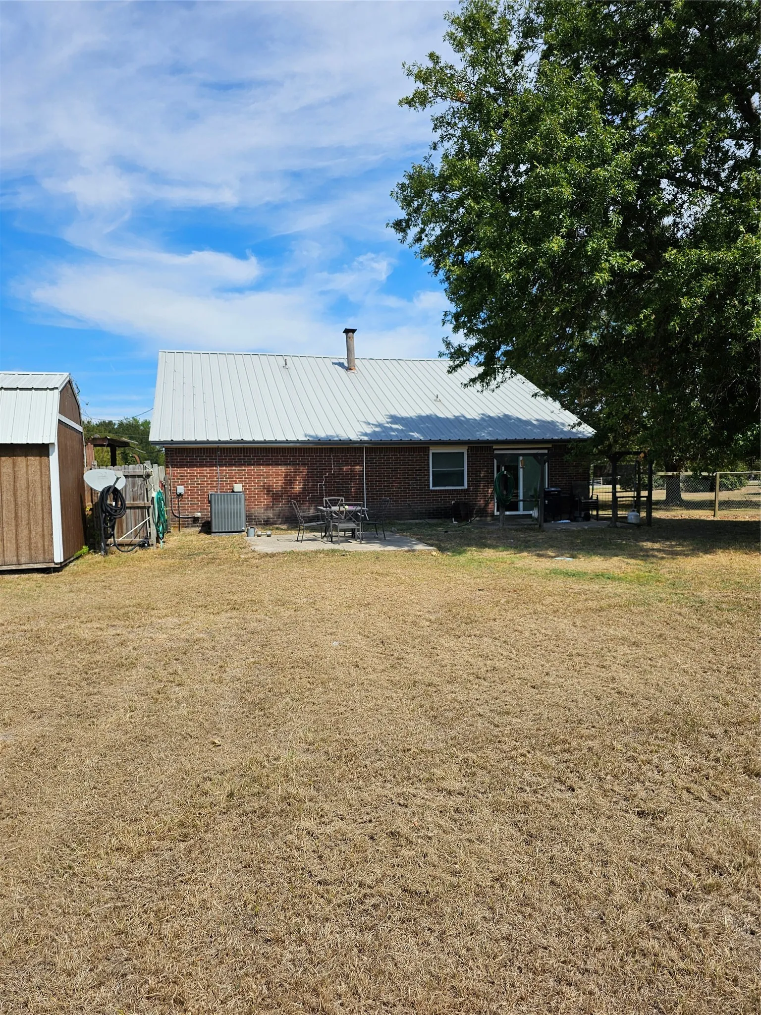 Brick exterior with a metal roof, outdoor patio area, and a detached storage shed