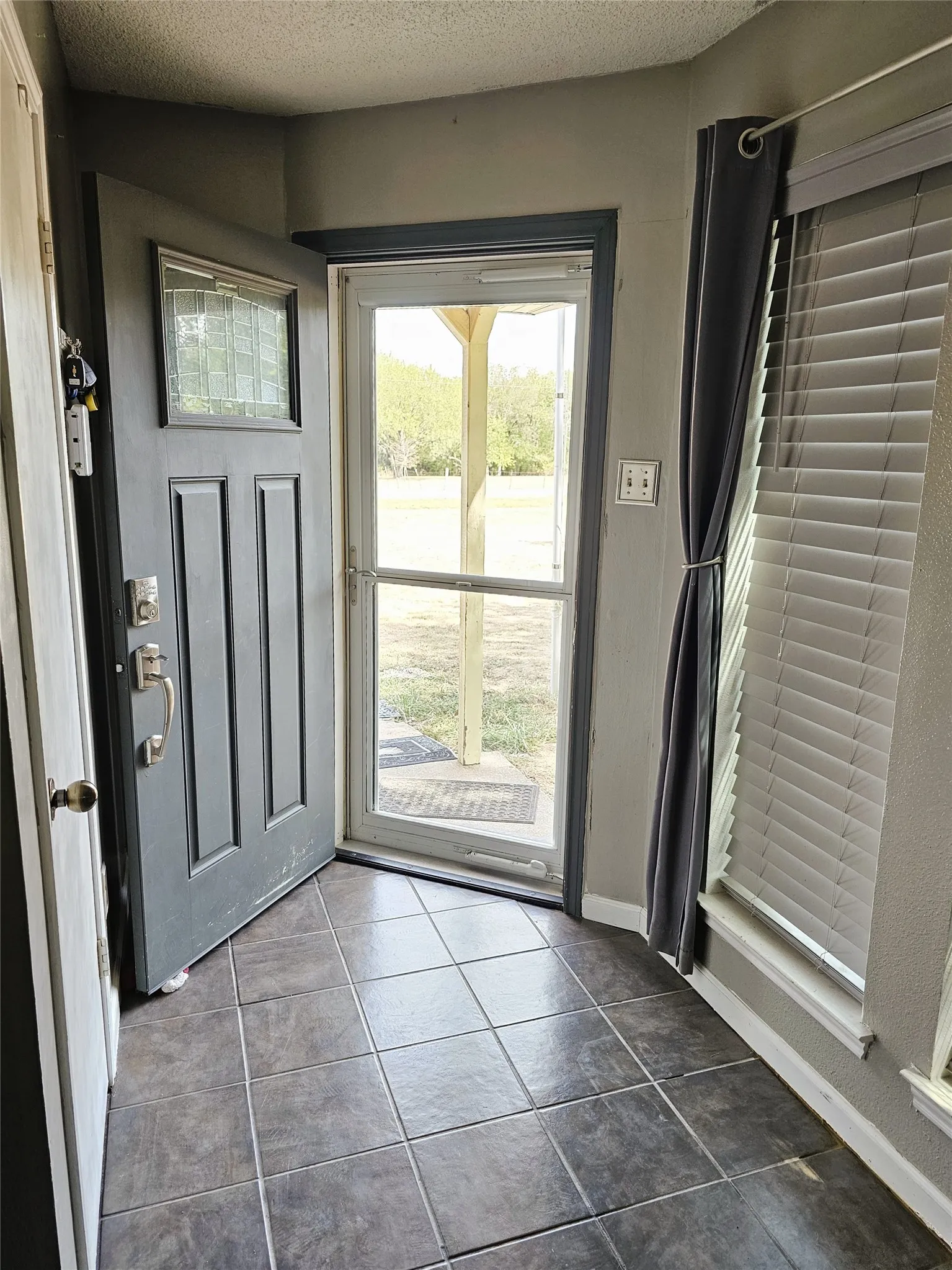 Tile flooring entryway with a storm door, window with blinds, and paneled entry door