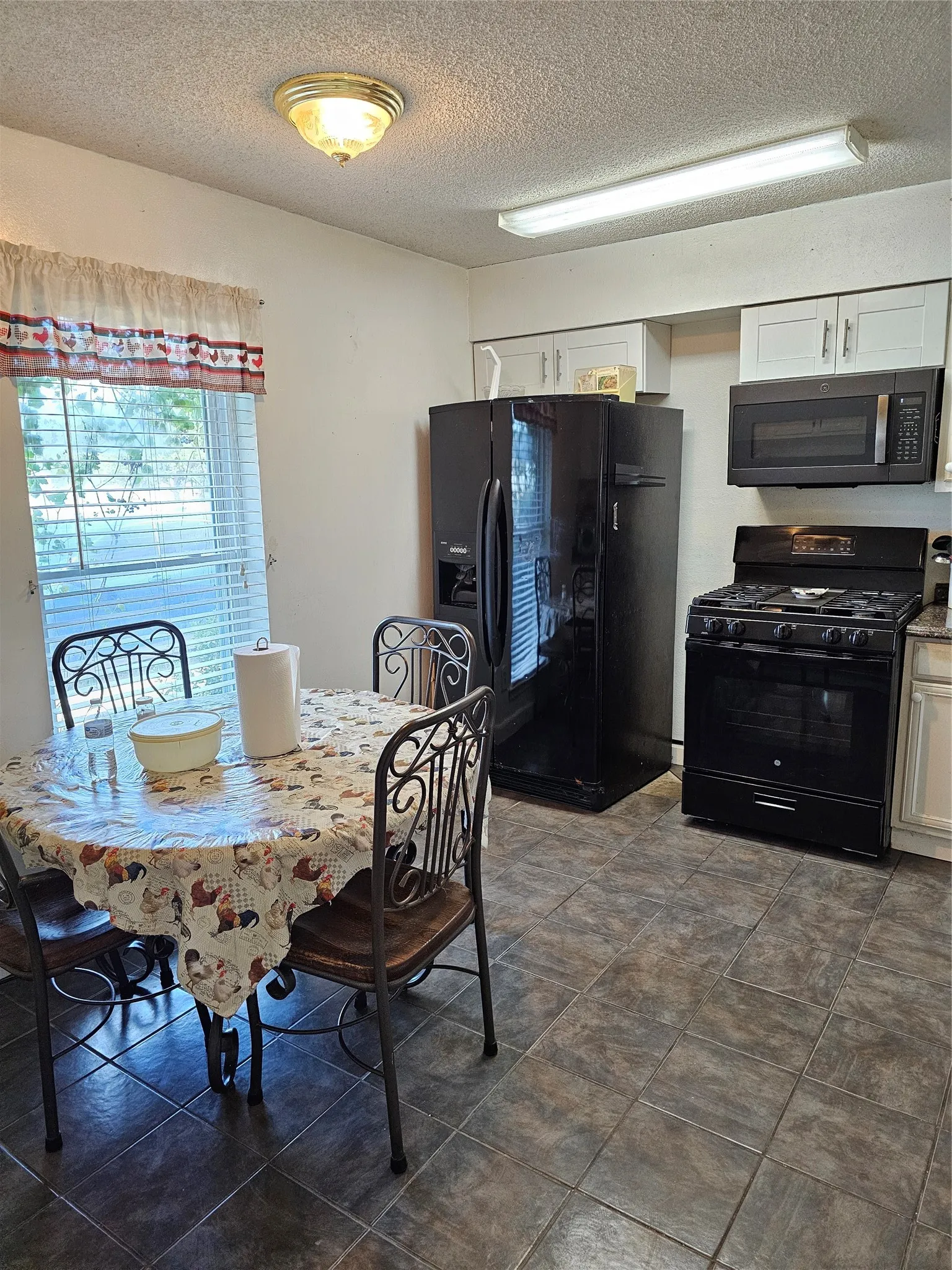 Kitchen featuring dark tile flooring, a window with blinds, and white cabinetry