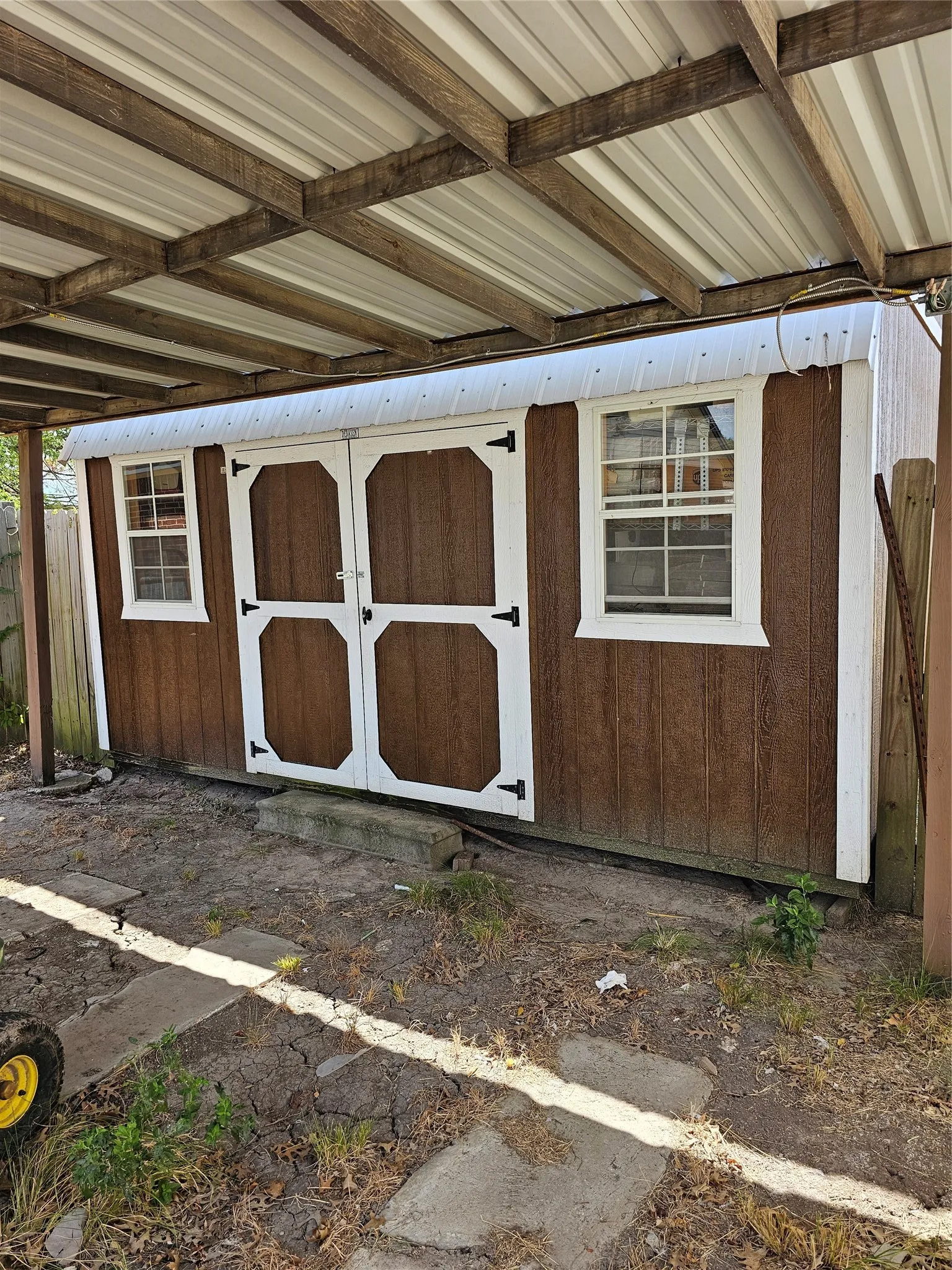 Storage shed featuring a metal roof, double doors, and two windows