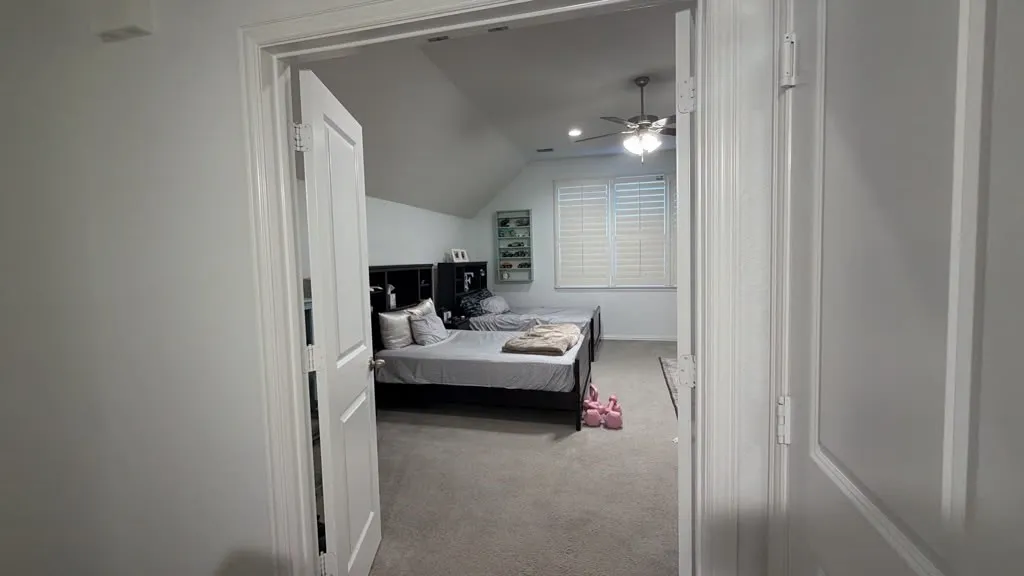 Room with sloped ceilings, ceiling fan, carpet flooring, and white window shutters