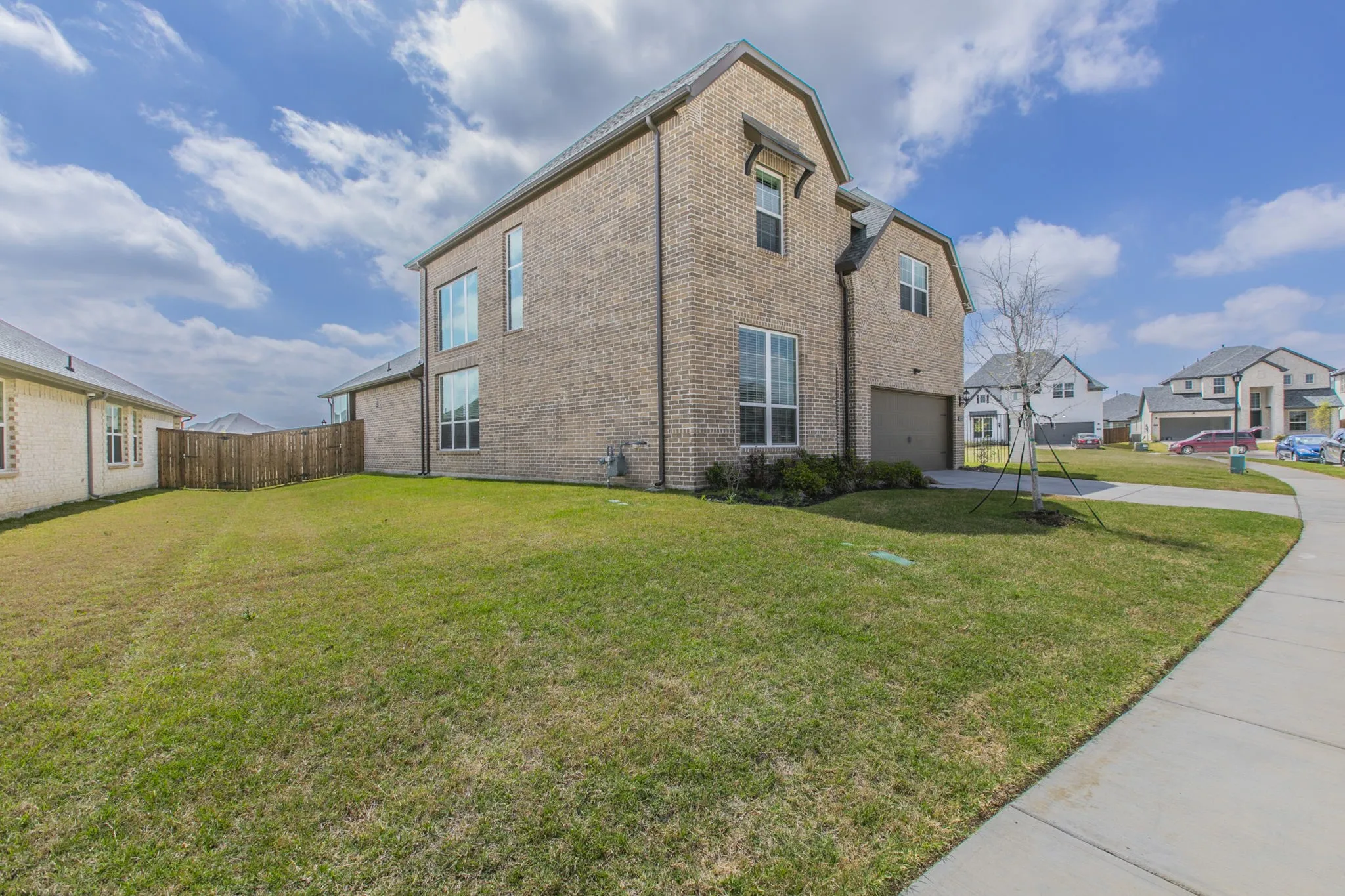 View of property exterior featuring brick siding, an attached garage, concrete driveway, and a residential view