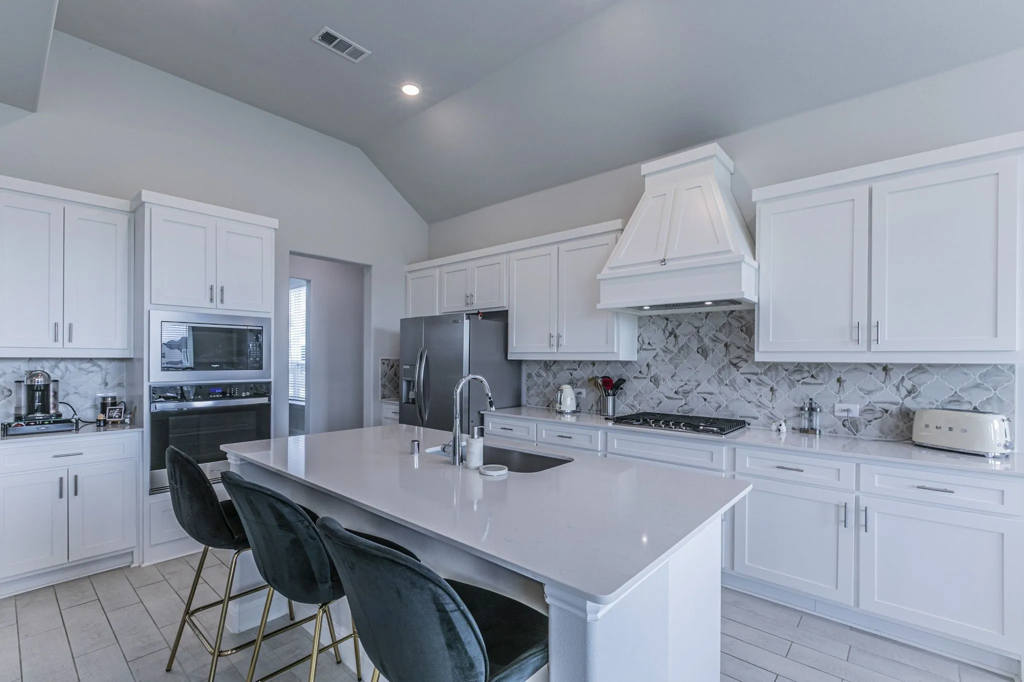Kitchen featuring a center island with sink, stainless steel appliances, lofted ceiling, white cabinets, and a breakfast bar