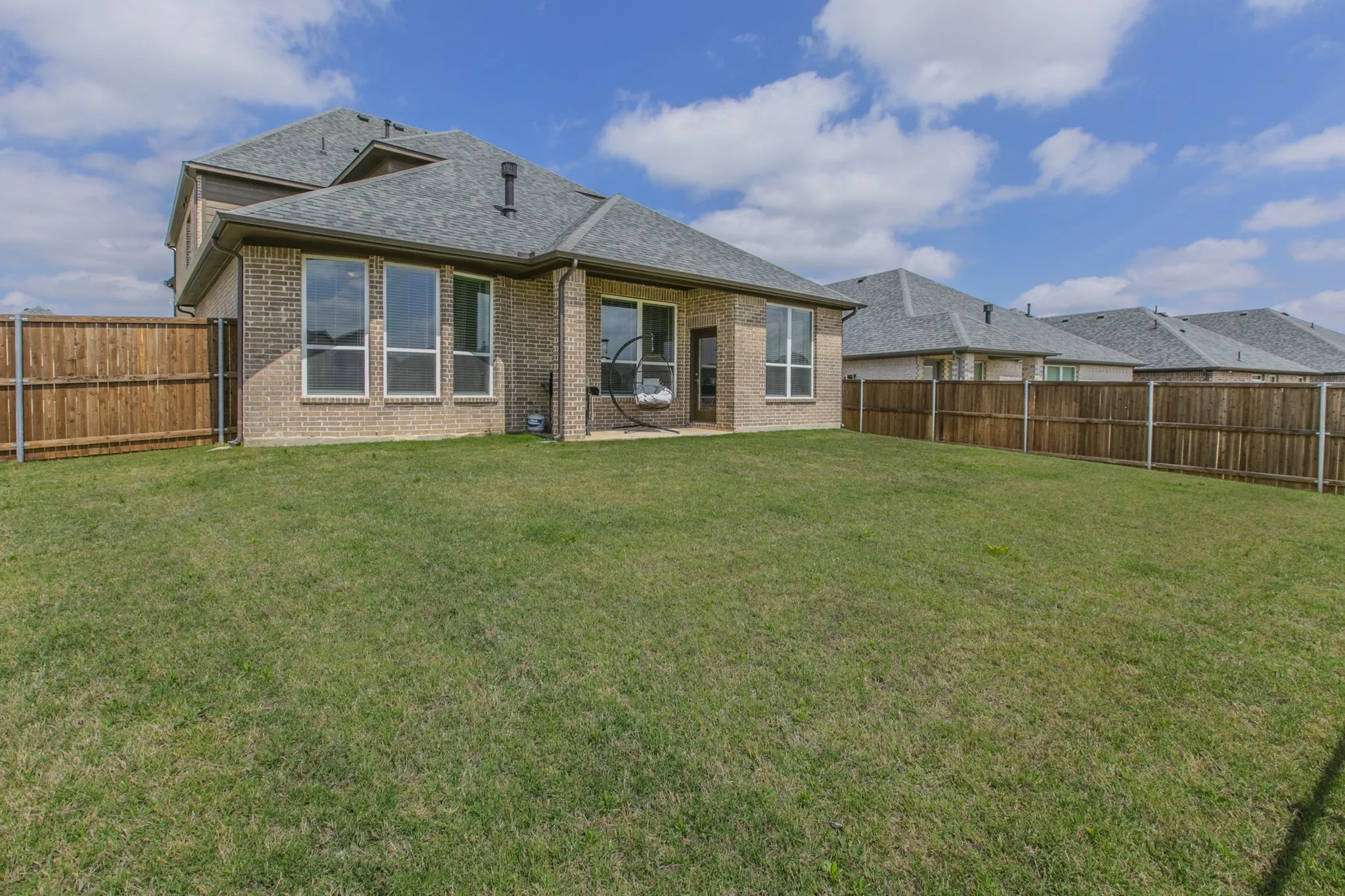 Back of property with brick siding, a shingled roof, a patio area, and a fenced backyard