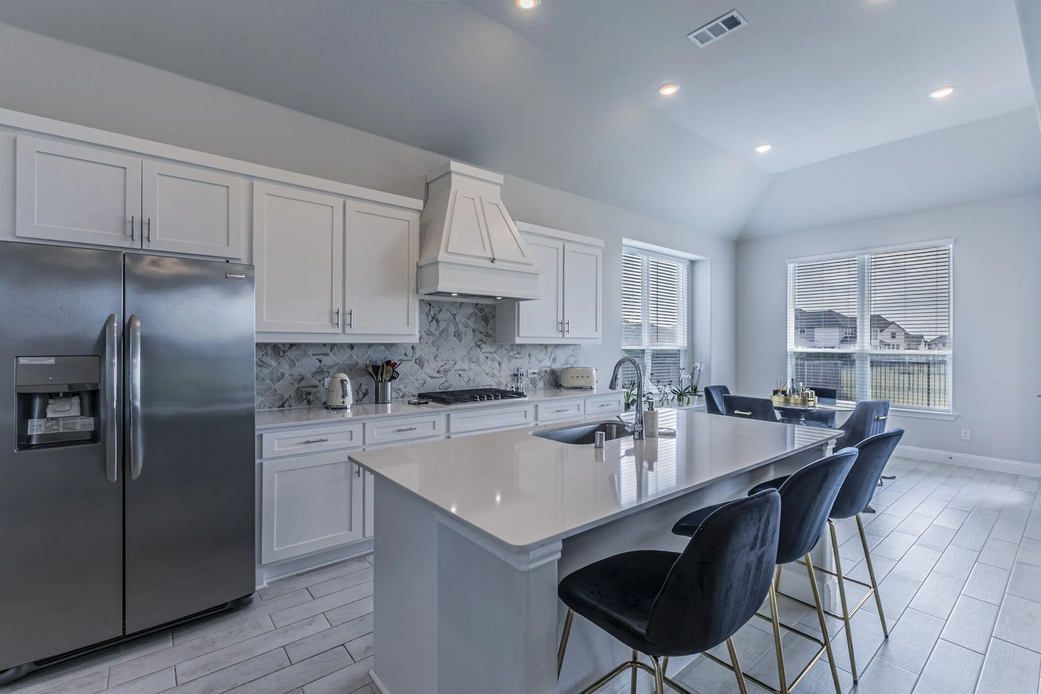 Kitchen with stainless steel built in refrigerator, wood finish floors, backsplash, light stone countertops, and lofted ceiling