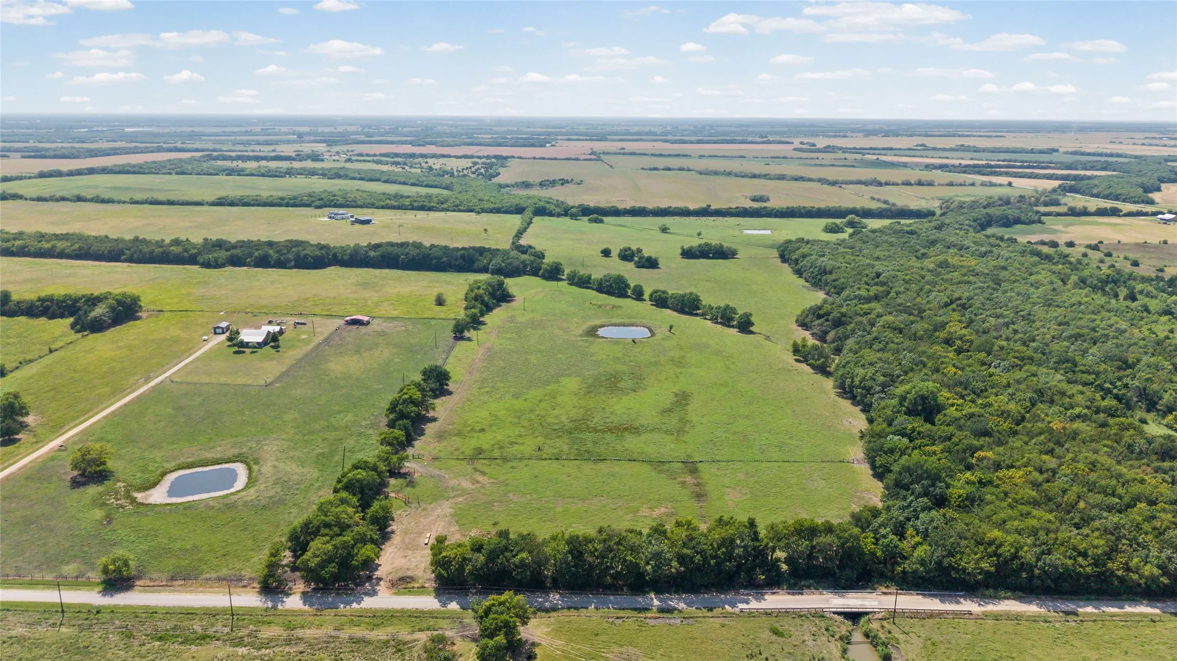 Expansive parcel featuring a mix of open fields and mature tree lines, multiple water features, and a residential structure with an accompanying outbuilding