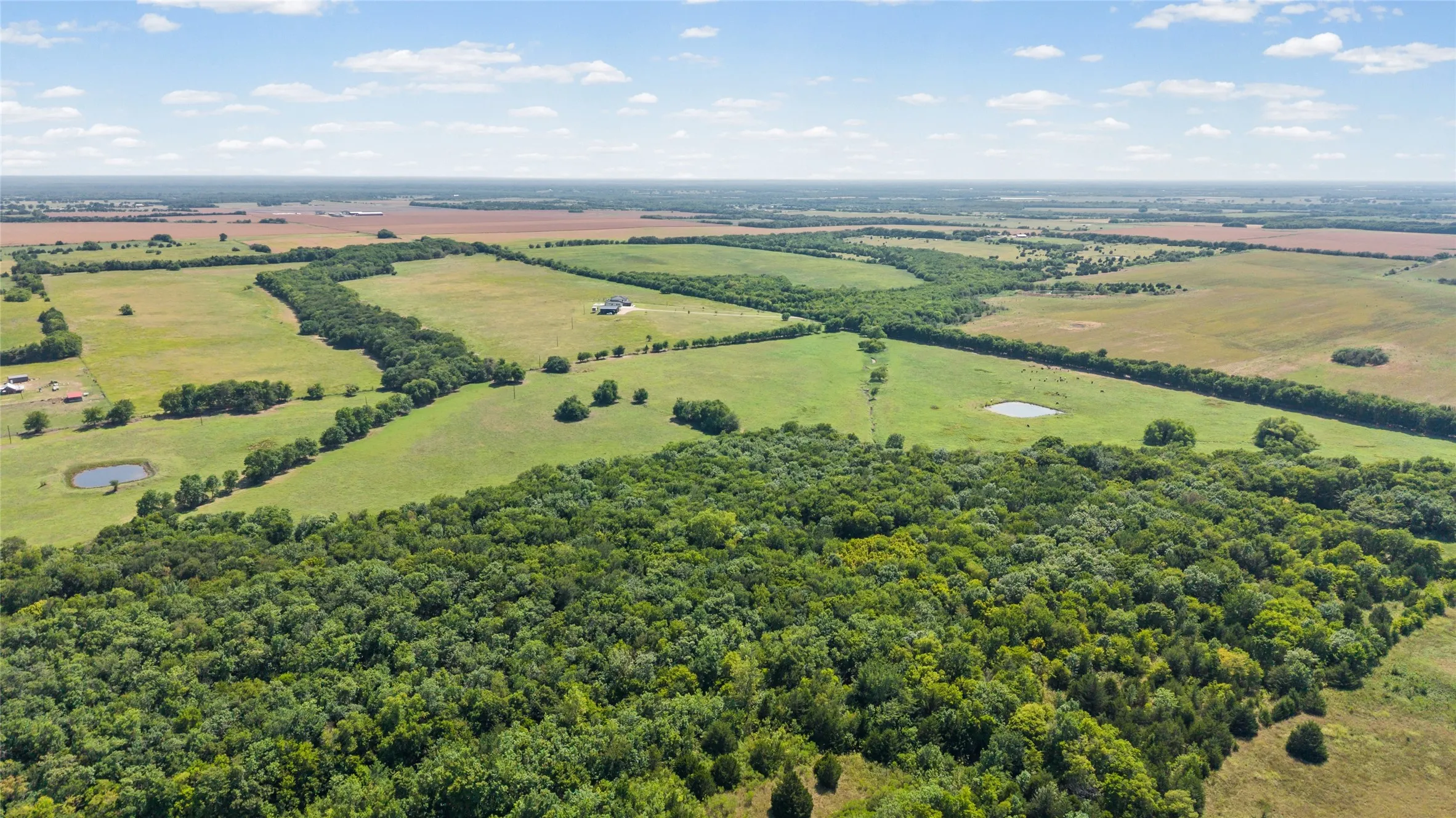 Expansive land featuring wooded areas, open fields, and multiple ponds