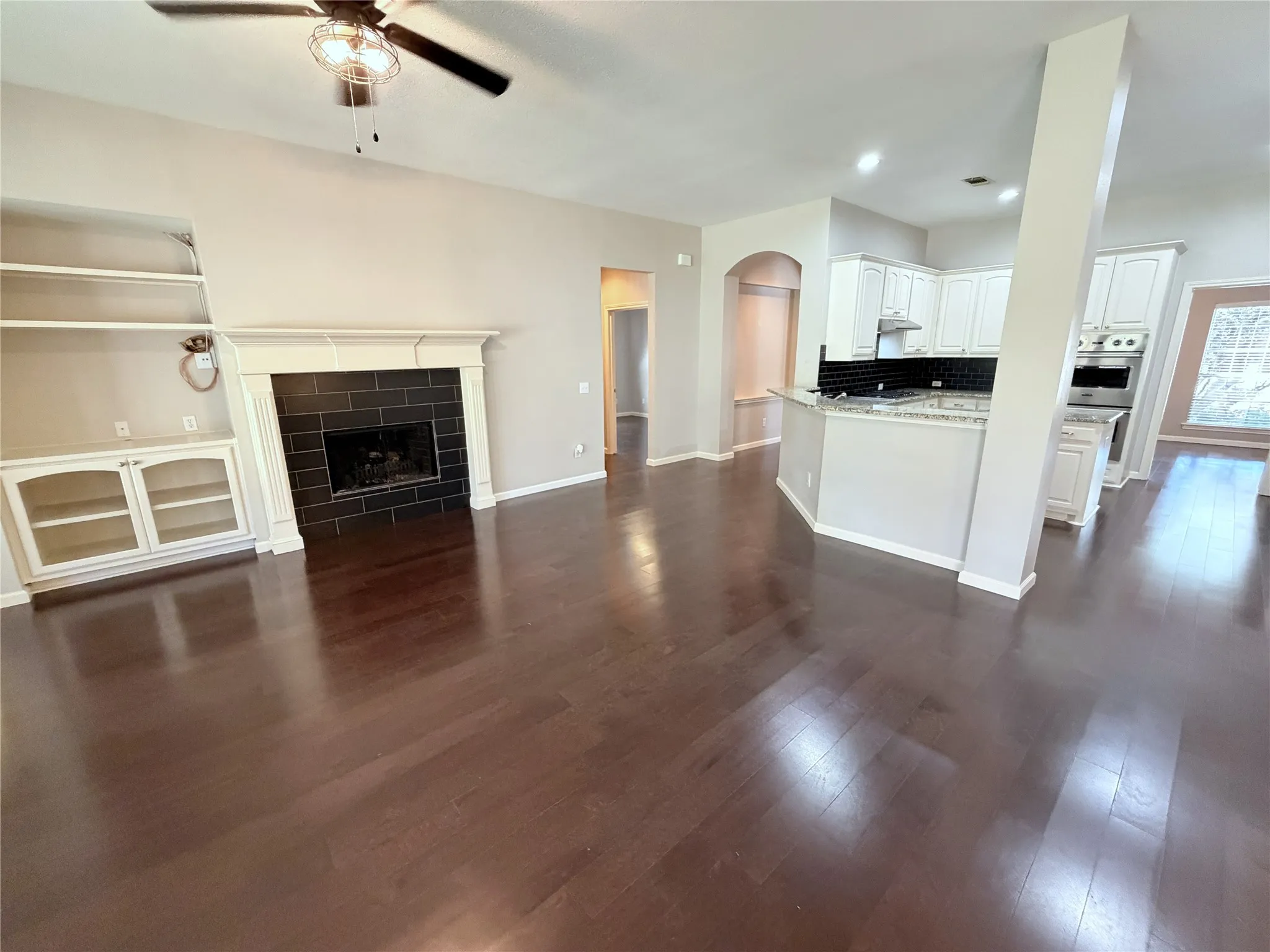 Dark wood-finish flooring, built-in shelving, white fireplace mantel with dark tile surround, white cabinetry, and recessed lighting