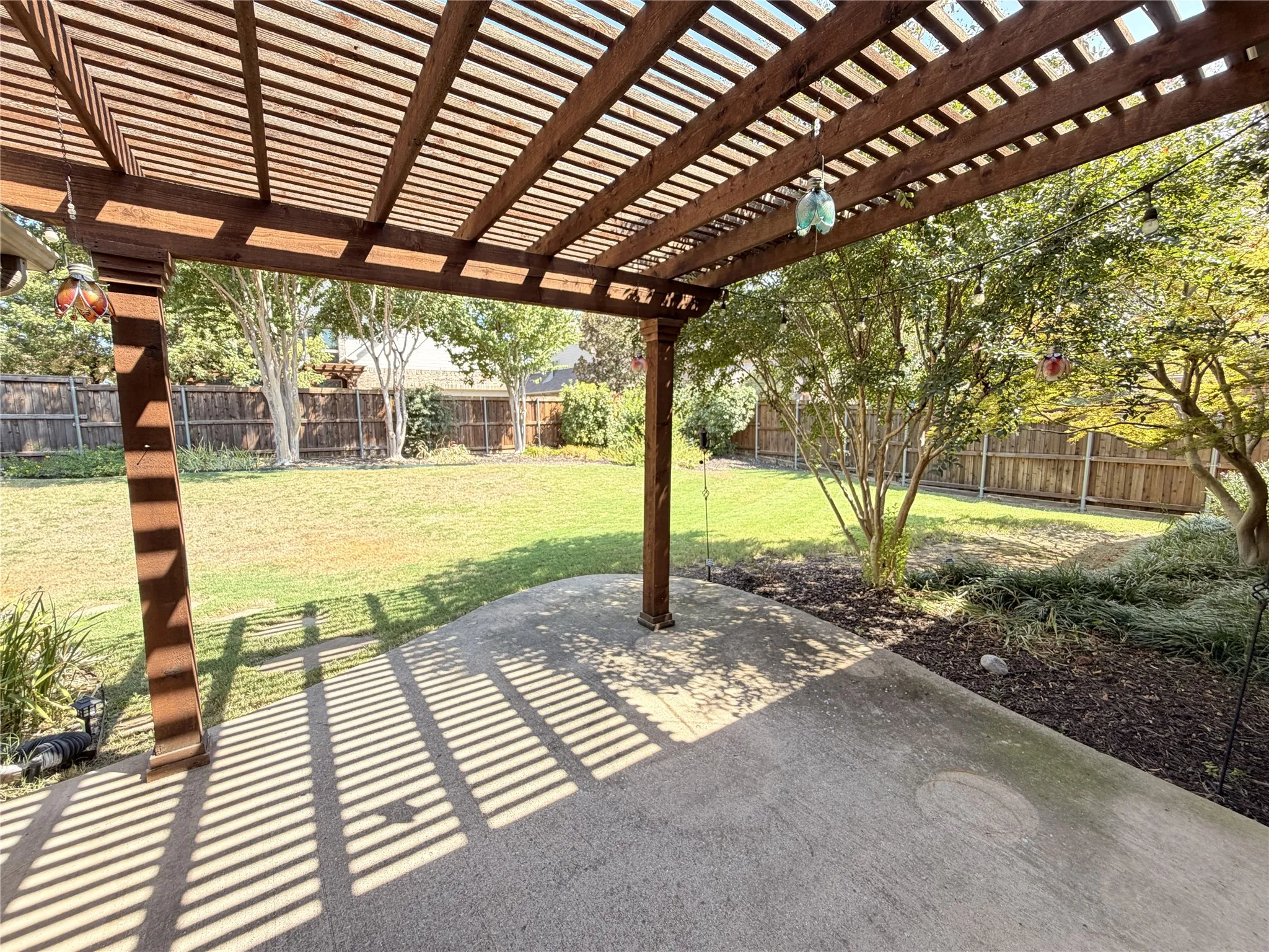 Expansive backyard featuring a wood pergola, concrete patio, mature trees, and a wooden fence
