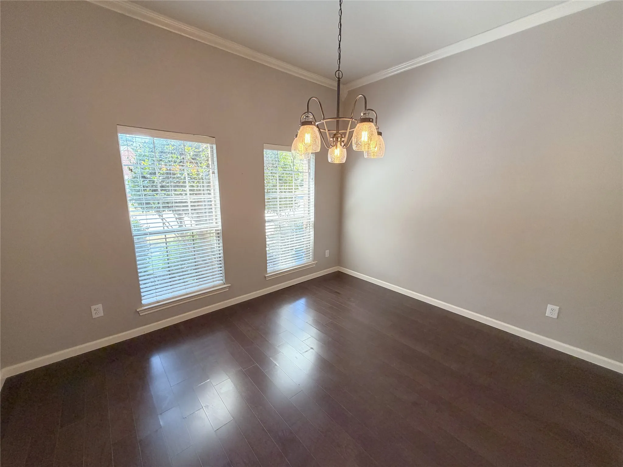 Hardwood-finish flooring, crown molding, two windows with blinds, and an overhead chandelier
