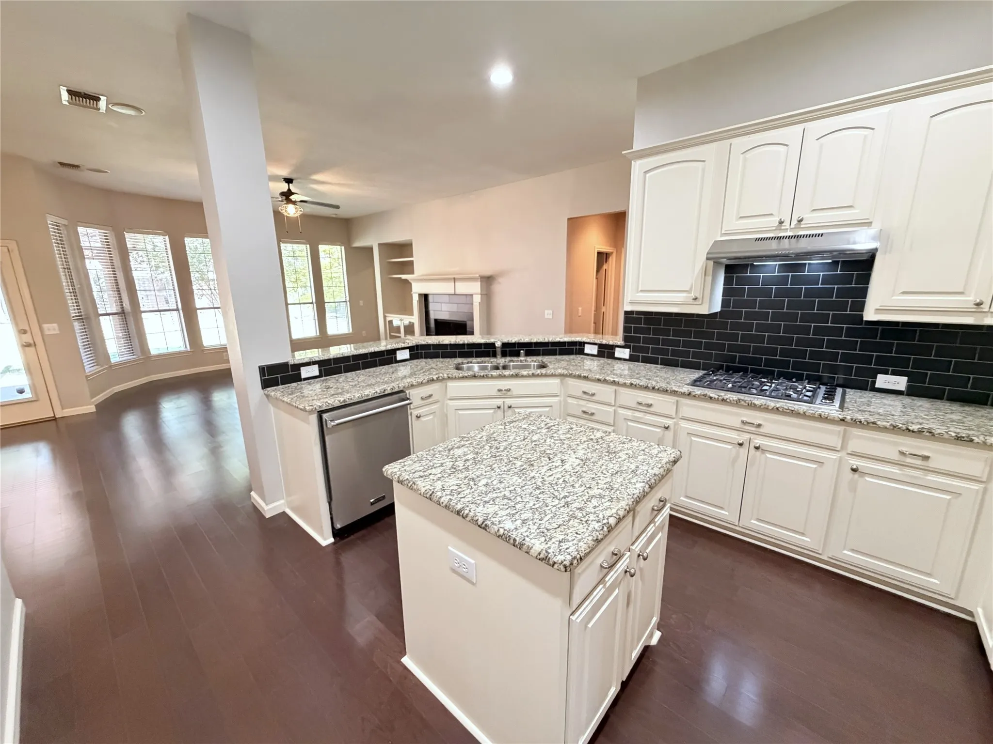 Kitchen featuring a central island, stainless steel appliances, white cabinetry, dark subway tile backsplash, and light-toned countertops