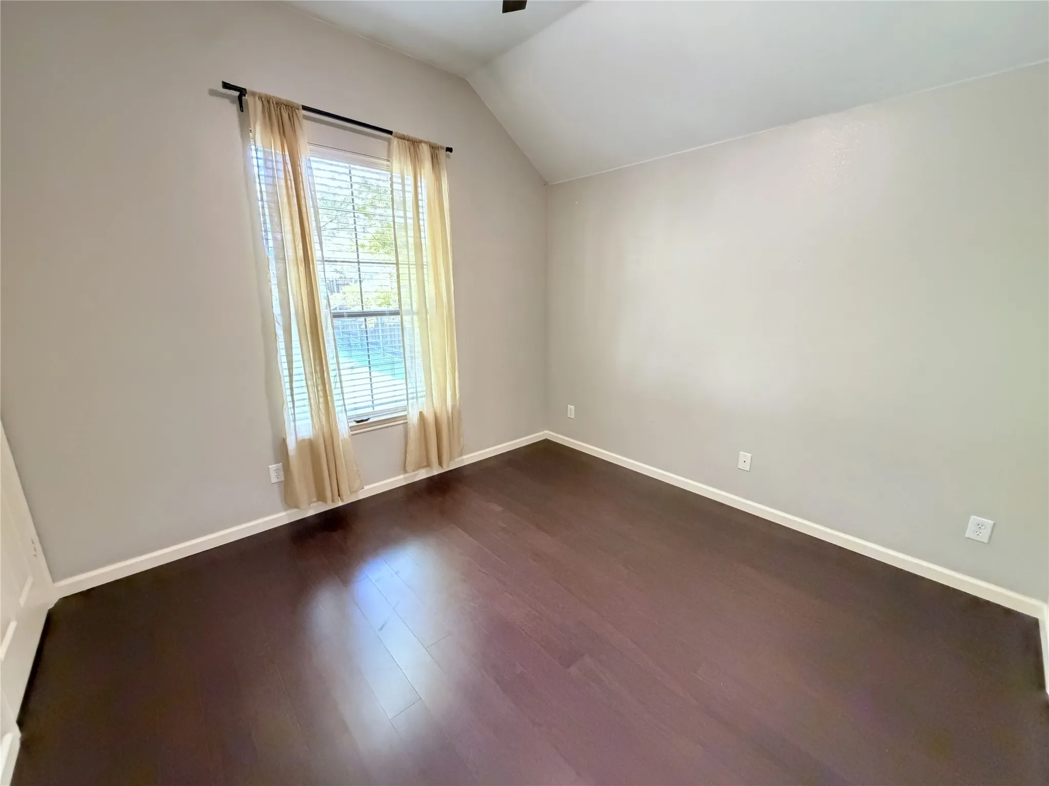 Vaulted ceiling, dark wood-finish flooring, neutral wall tones, window with blinds