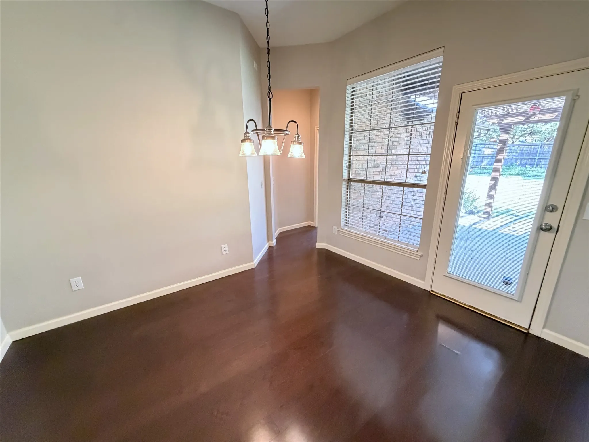 Wood-finish flooring, full-light exterior door, window with blinds, and a multi-light chandelier