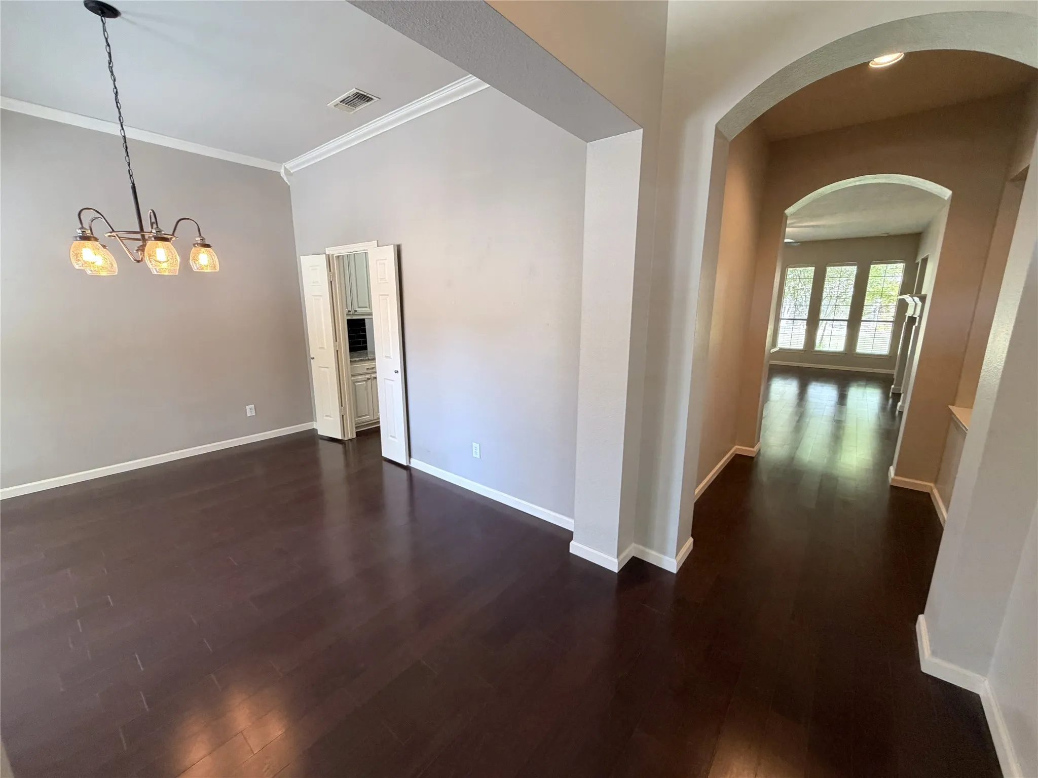Dark wood-finish flooring throughout, vaulted ceiling, crown molding, and an arched entry
