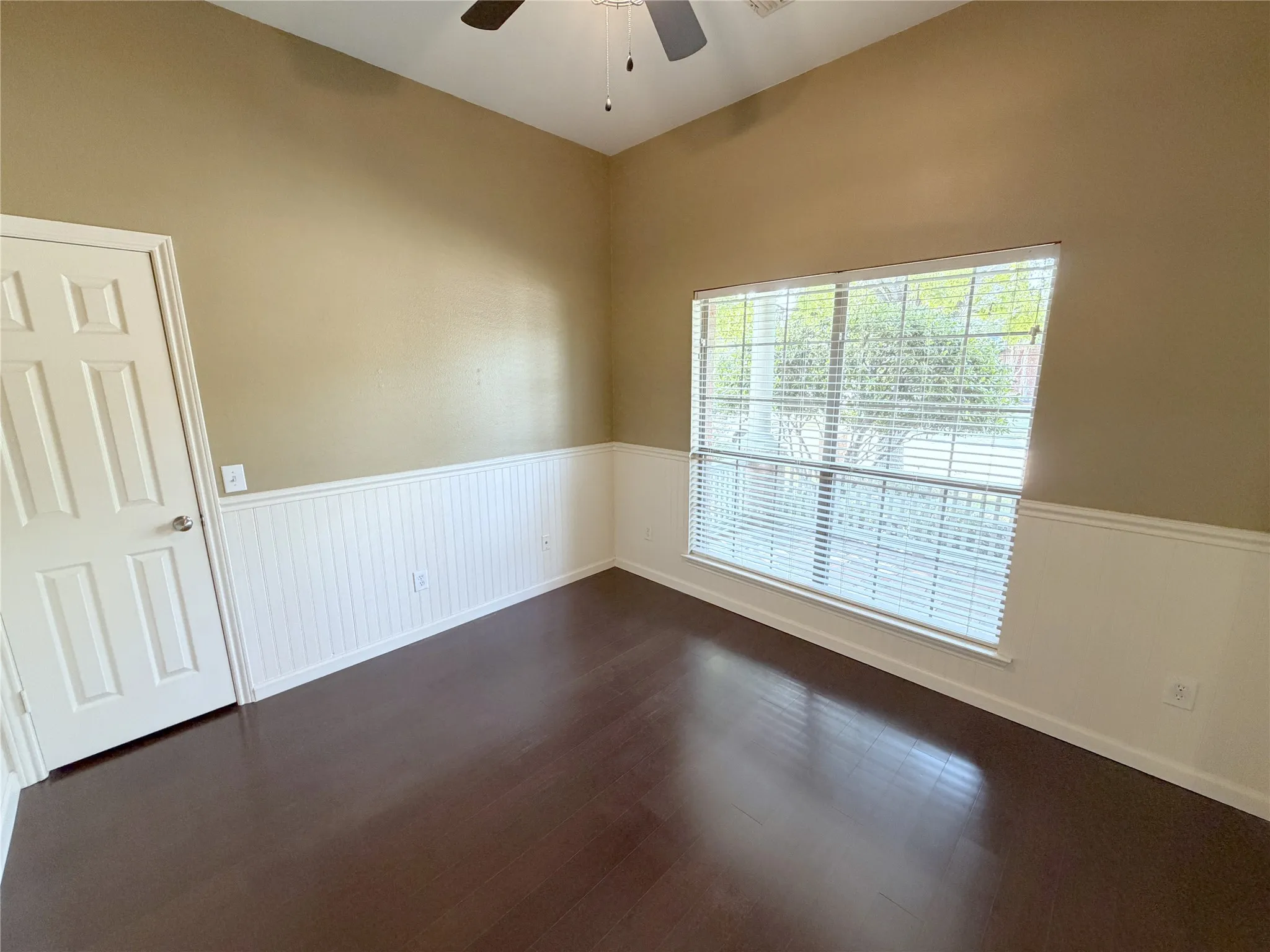 Vaulted ceiling with an attached ceiling fan, wood-finish flooring, and panel wainscoting