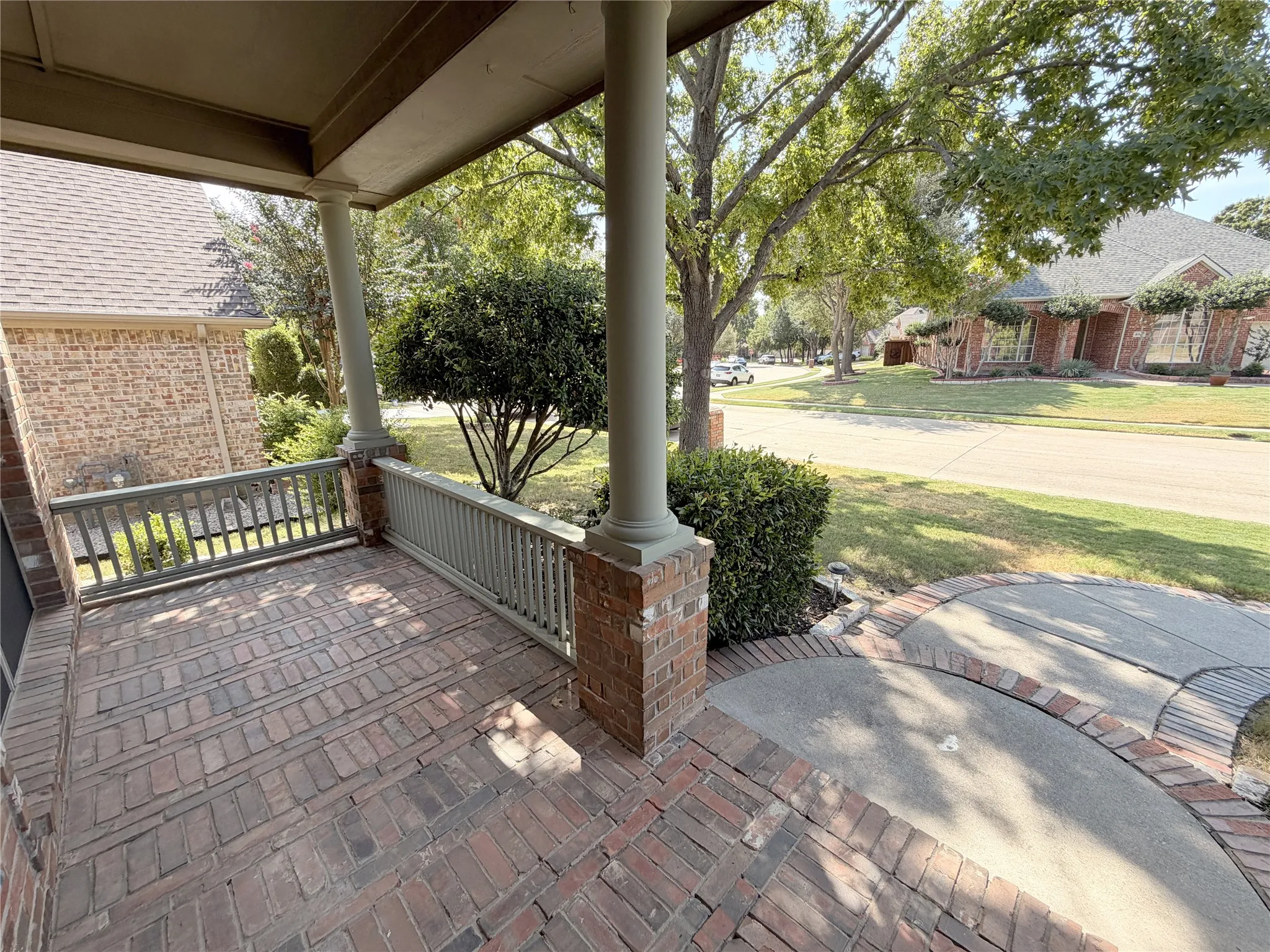 Brick-paved front porch with painted railings, brick columns, and a landscaped front yard